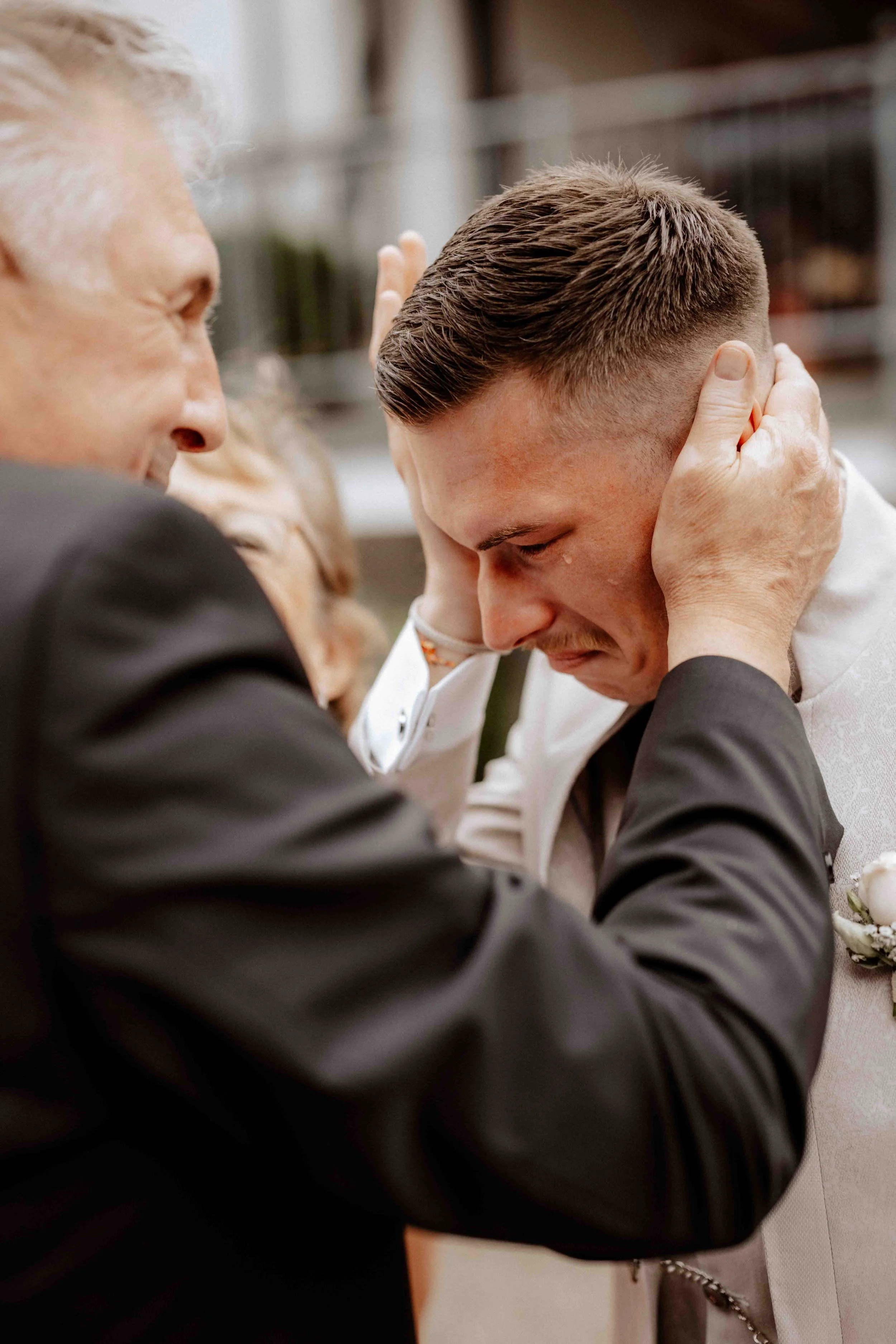 Ein junger Mann wird von einem älteren Mann emotional getröstet. Er trägt einen weißen Anzug, er scheint sich an einem besonderen Moment zu befinden. Es ist der Bräutigam der Hochzeit welche in Wipperfürth bei Köln im Landgut Stüttem stattfindet. 