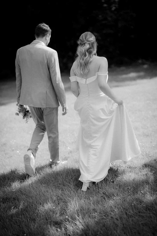 Ein Paar in Hochzeitskleidung läuft auf einer Wiese bei Sonnenuntergang, im Hintergrund Bäume, die Szene ist schwarz-weiß. Die Hochzeit findet in Düsseldorf, Nähe Köln statt. 