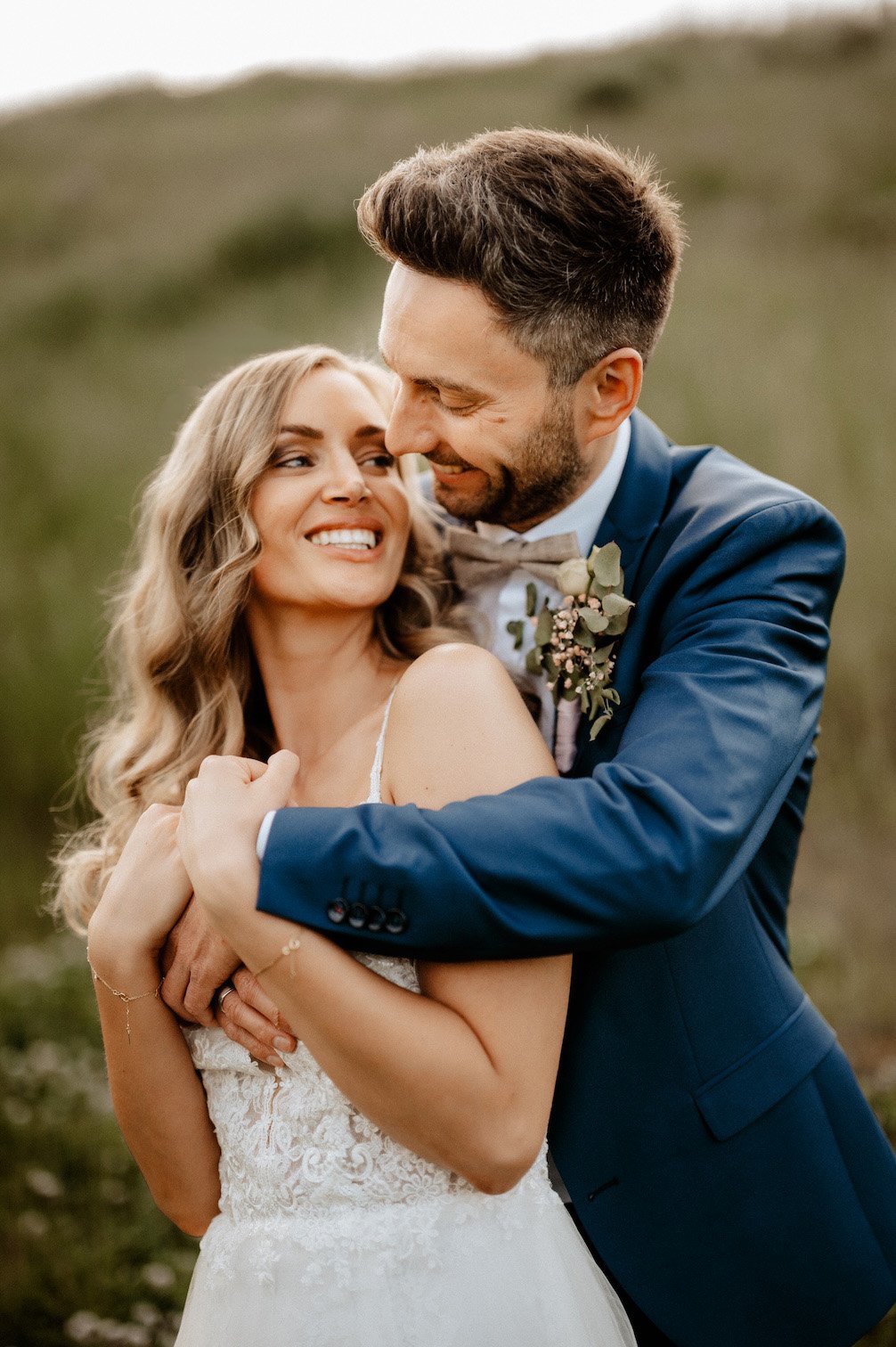 Ein glückliches Brautpaar umarmt sich draußen bei Sonnenuntergang, lachend. Das Brautpaar befindet sich in Köln, NRW, Deutschland. 