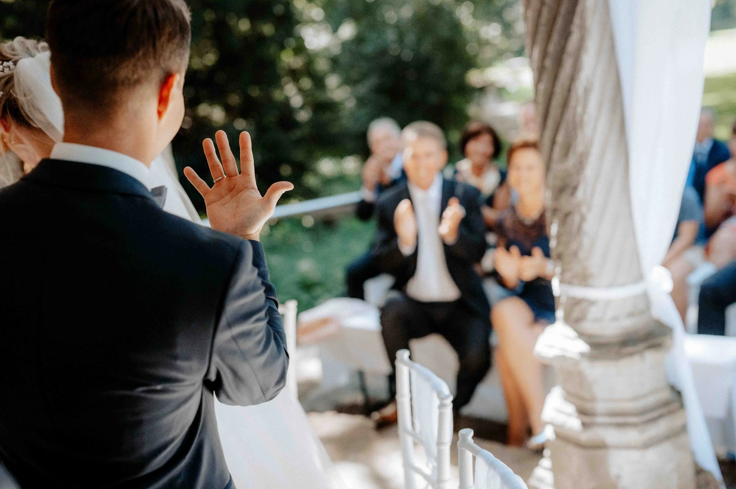 Ein Mann im Anzug winkt einem Brautpaar bei einer Hochzeit im Freien. Die Hochzeit findet im Schloss Paffendorf in Bergheim, Nähe Köln statt. 