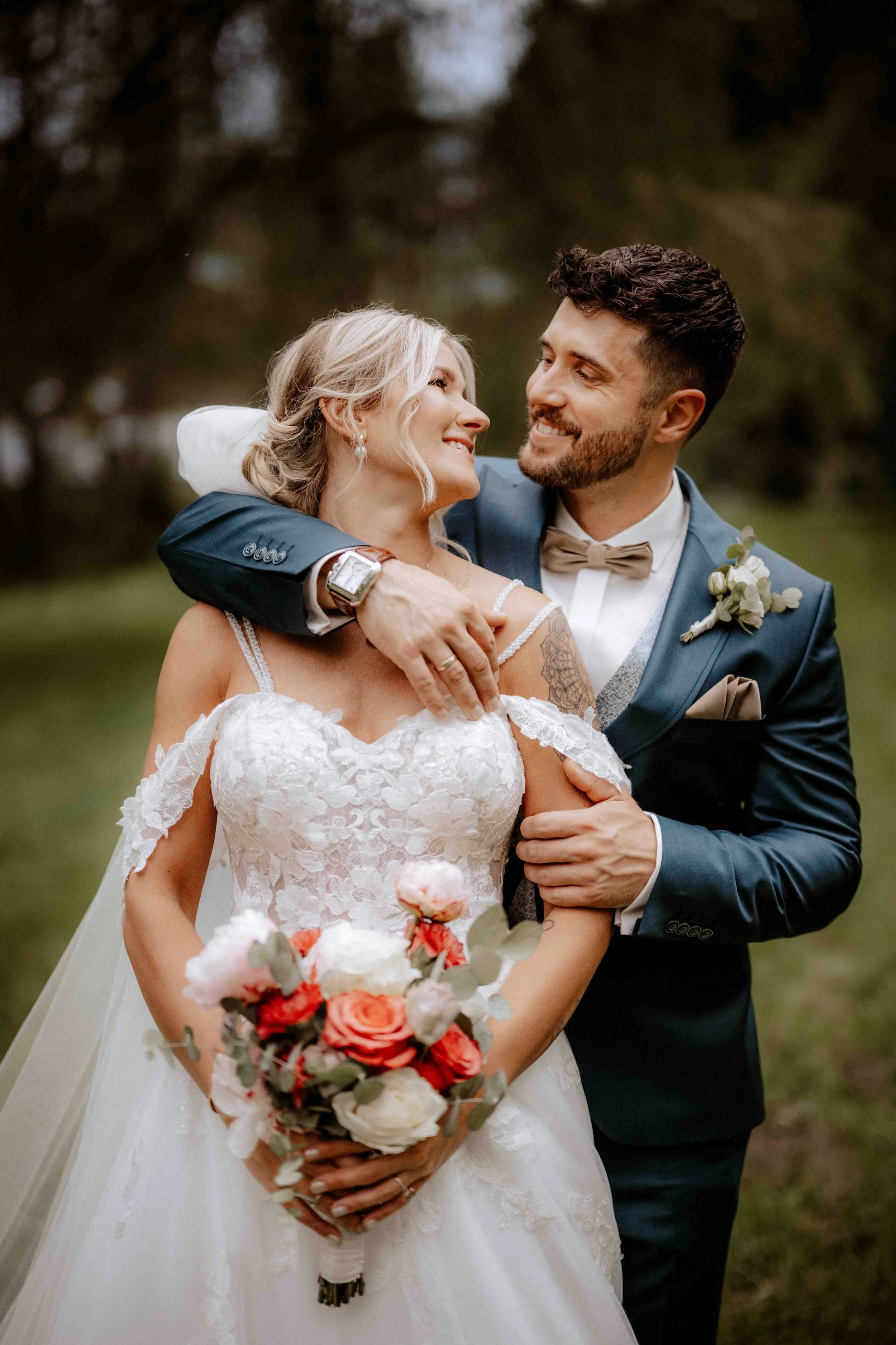 Ein Mann und eine Frau, vermutlich Braut und Bräutigam, beim Hochzeitsspaziergang im Freien, die Frau hält einen Blumenstrauß, beide lächeln sich liebevoll an. Die Hochzeit findet in Düsseldorf, Nähe Köln statt. 