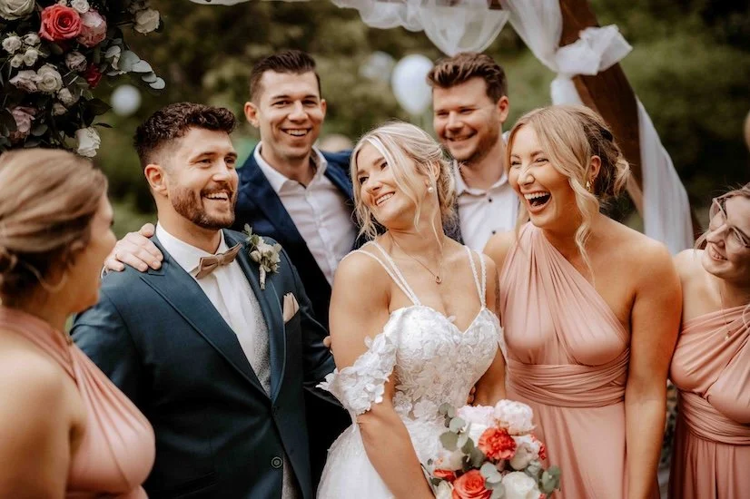 Hochzeitspaar mit Brautjungfern und Trauzeugen, lachend im Freien bei einer Hochzeit. Die Hochzeit findet in Düsseldorf, Nähe Köln statt. 