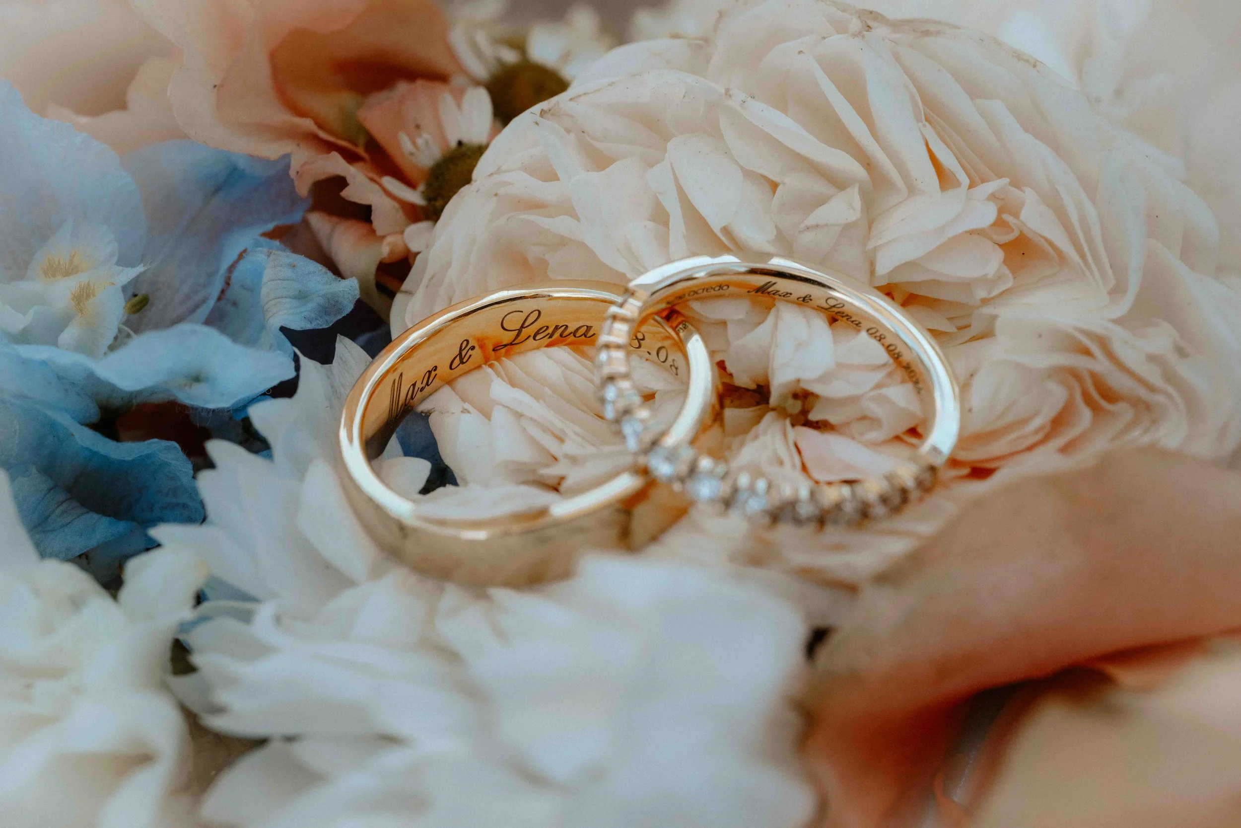 Zwei Eheringe liegen auf Blumen, einer ist schlicht und der andere mit Diamanten verschönert. Die Hochzeit findet in Düsseldorf, Nähe Köln statt. 