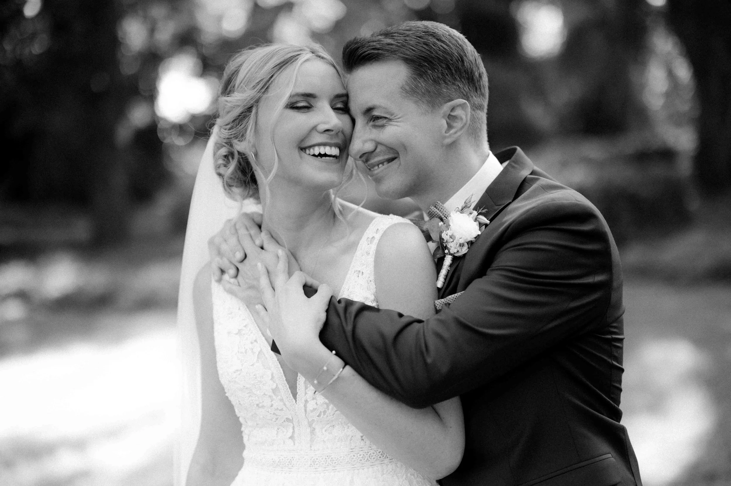 Ein lachendes Brautpaar bei einer Hochzeit, schwarz-weiß, umarmend im Freien. Der Ort ist das Schloss Paffendorf in Bedburg, in der Nähe von Köln und Düsseldorf.