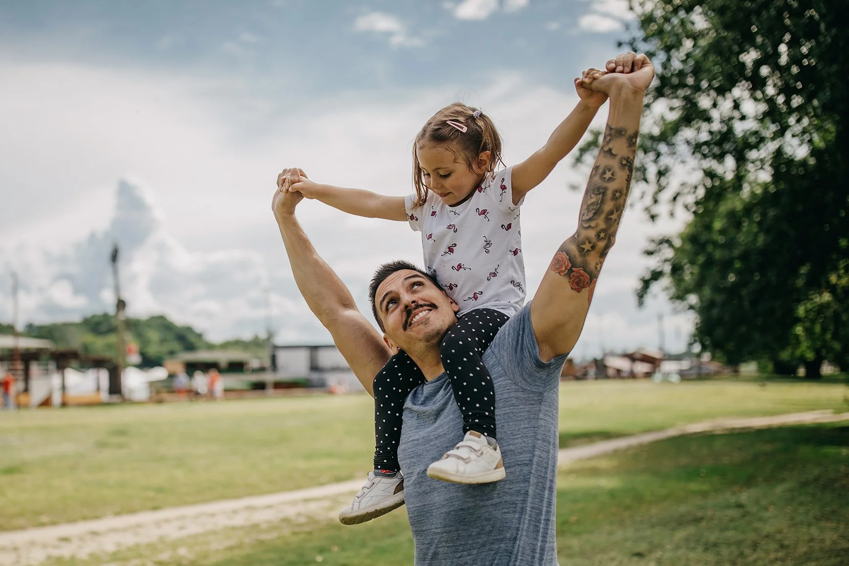 Father with his young daughter riding on his shoulders. They are playing in the park on a sunny, warm day.