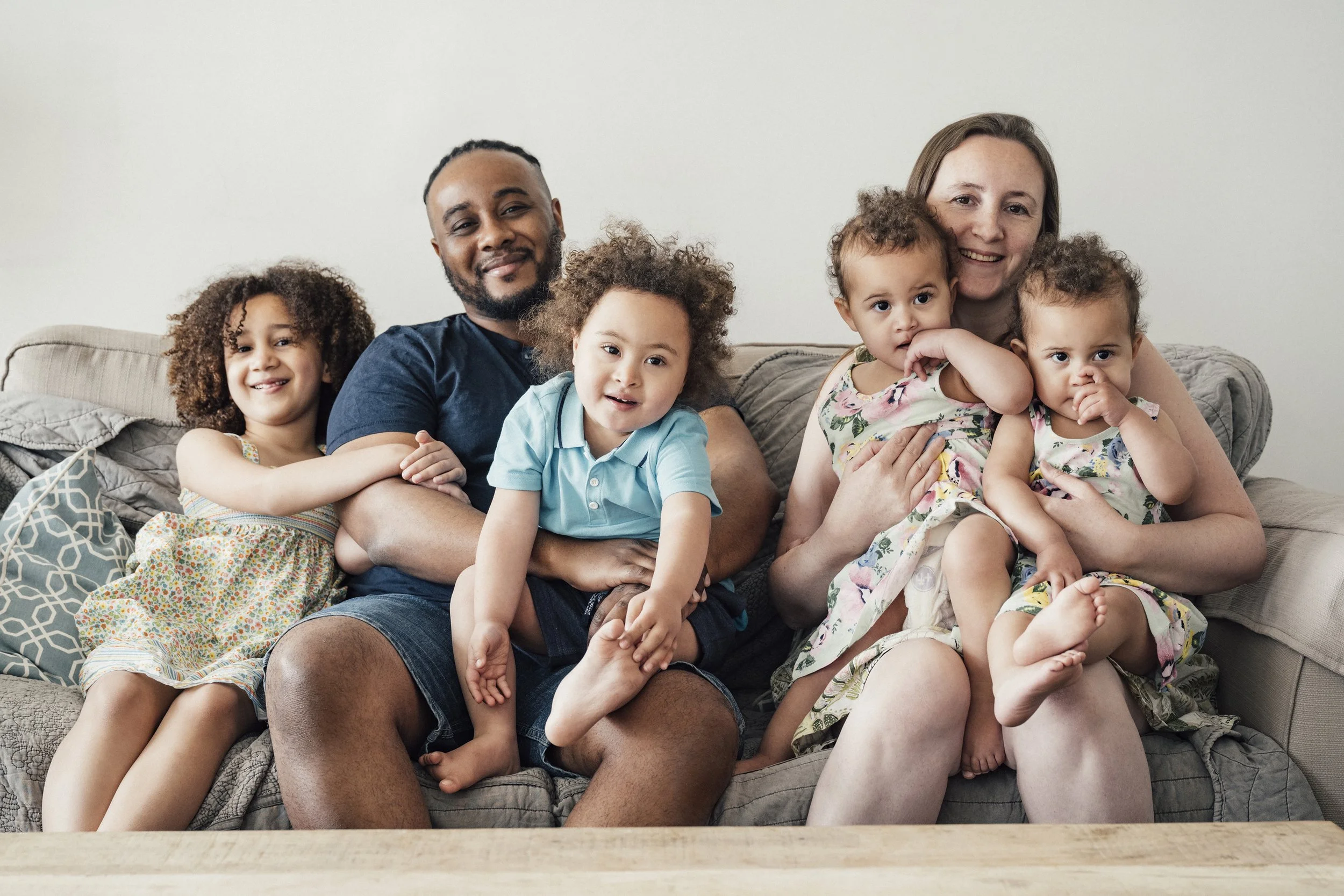 Portrait of a smiling family posed together with their four children on their couch.