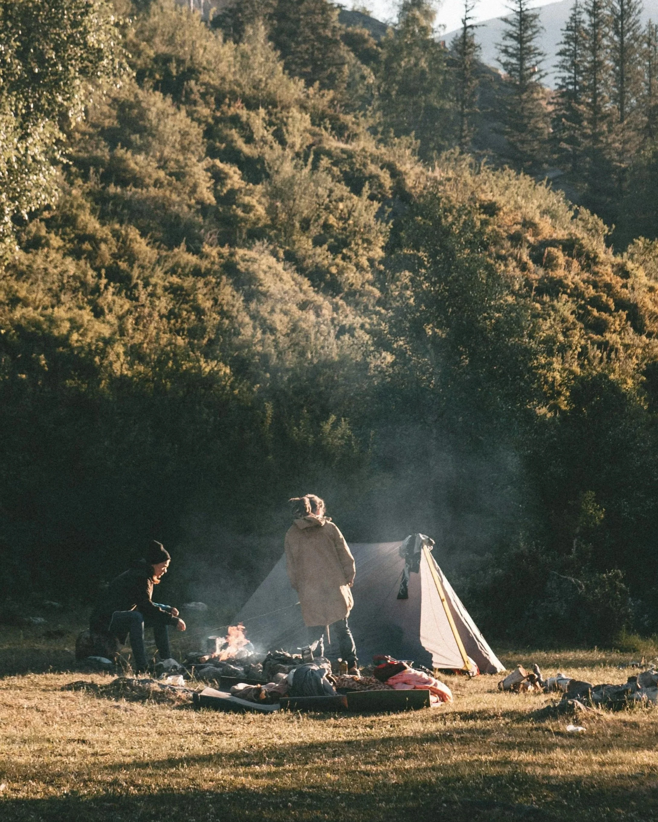 two people at a morning campfire next to a tent