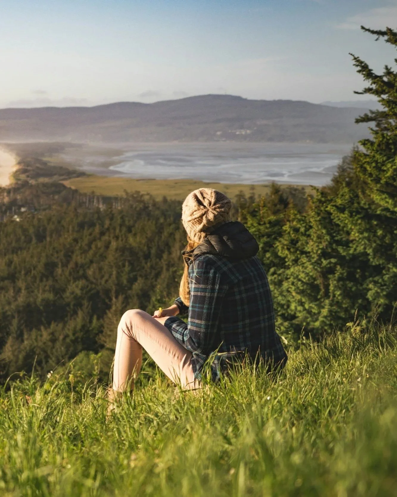 woman sitting on a grassy hill overlooking a valley