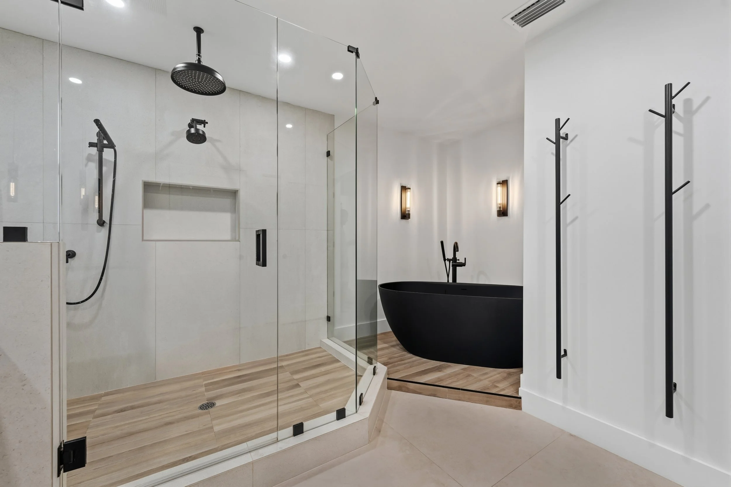 Modern bathroom with walk-in shower, black oval bathtub, and wall-mounted black towel racks.