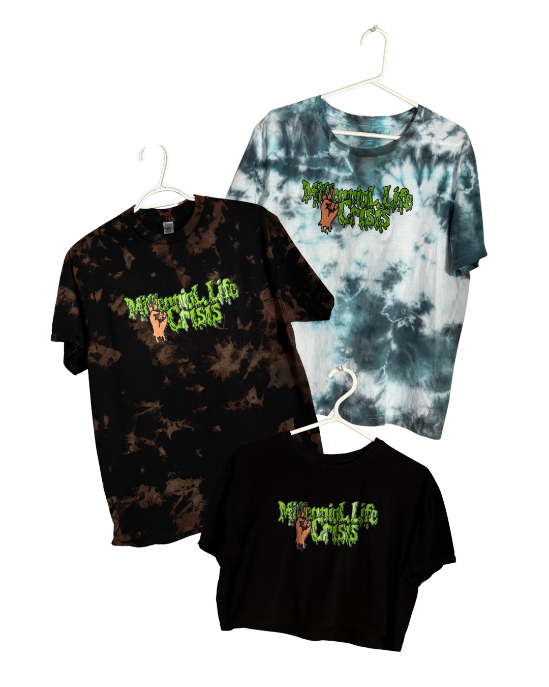 Three tie-dye t-shirts with the phrase 'Millennial Life Crisis' and a graphic of a hand making a peace sign hanging on white hangers.