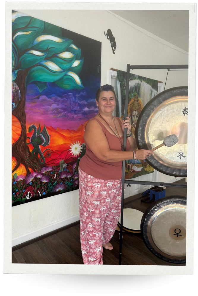 Woman standing in front of a vibrant painting and gongs, smiling at camera