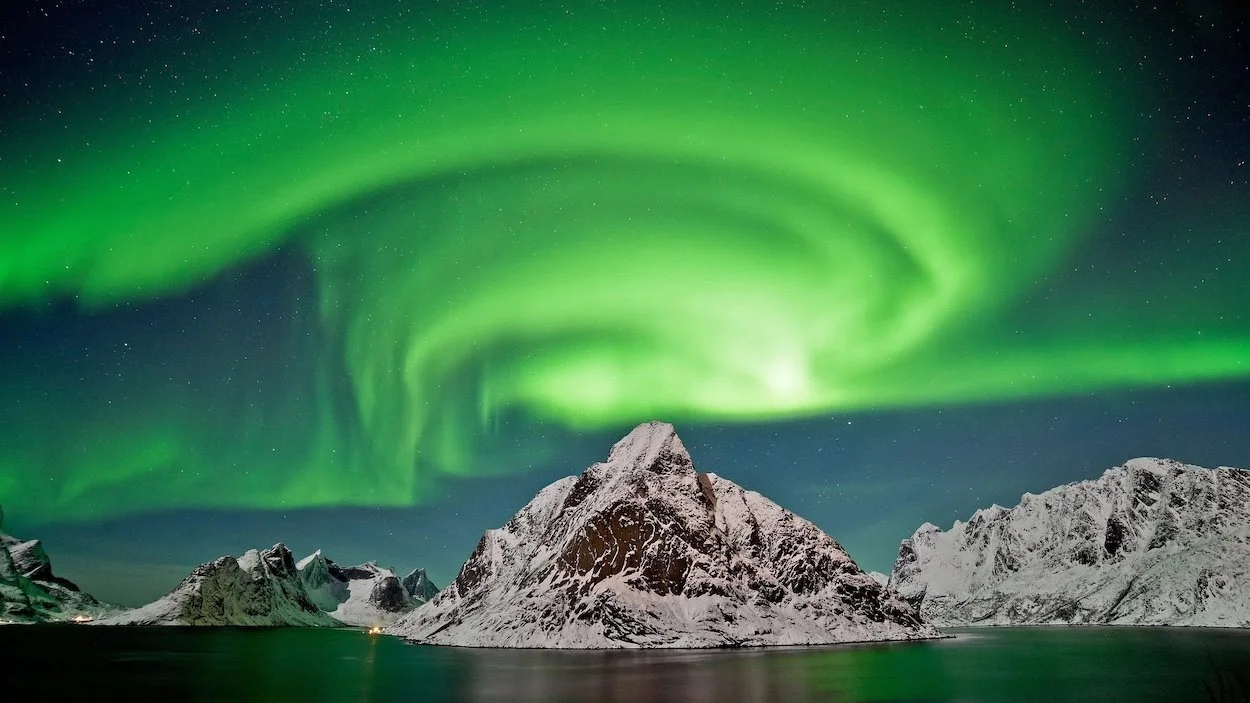green aurora borealis over snow covered mountains