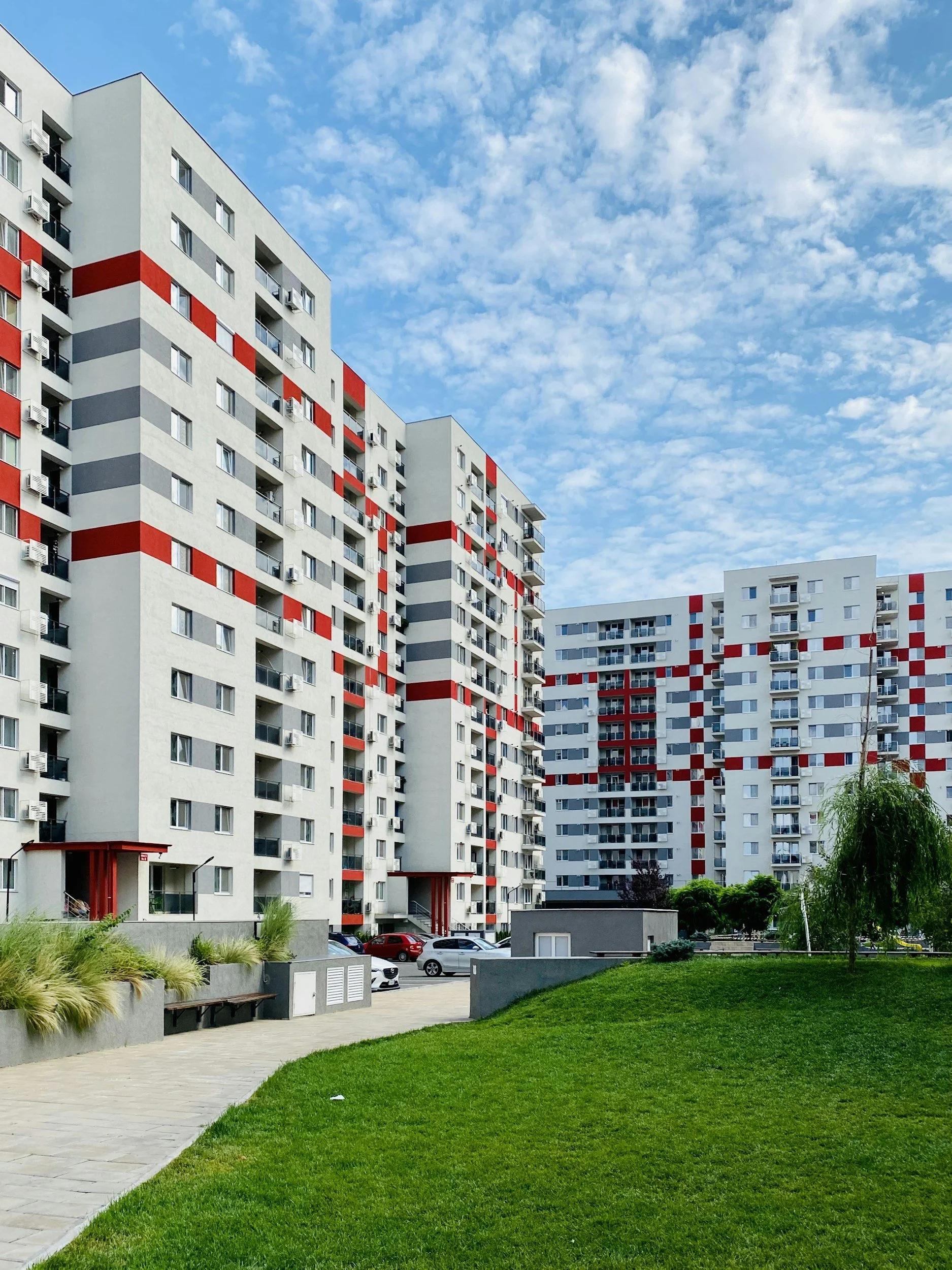 Modern white apartment buildings, a green lawn, and a cloudy blue sky. A beautiful and clean community enjoying the benefits of trash valet service.