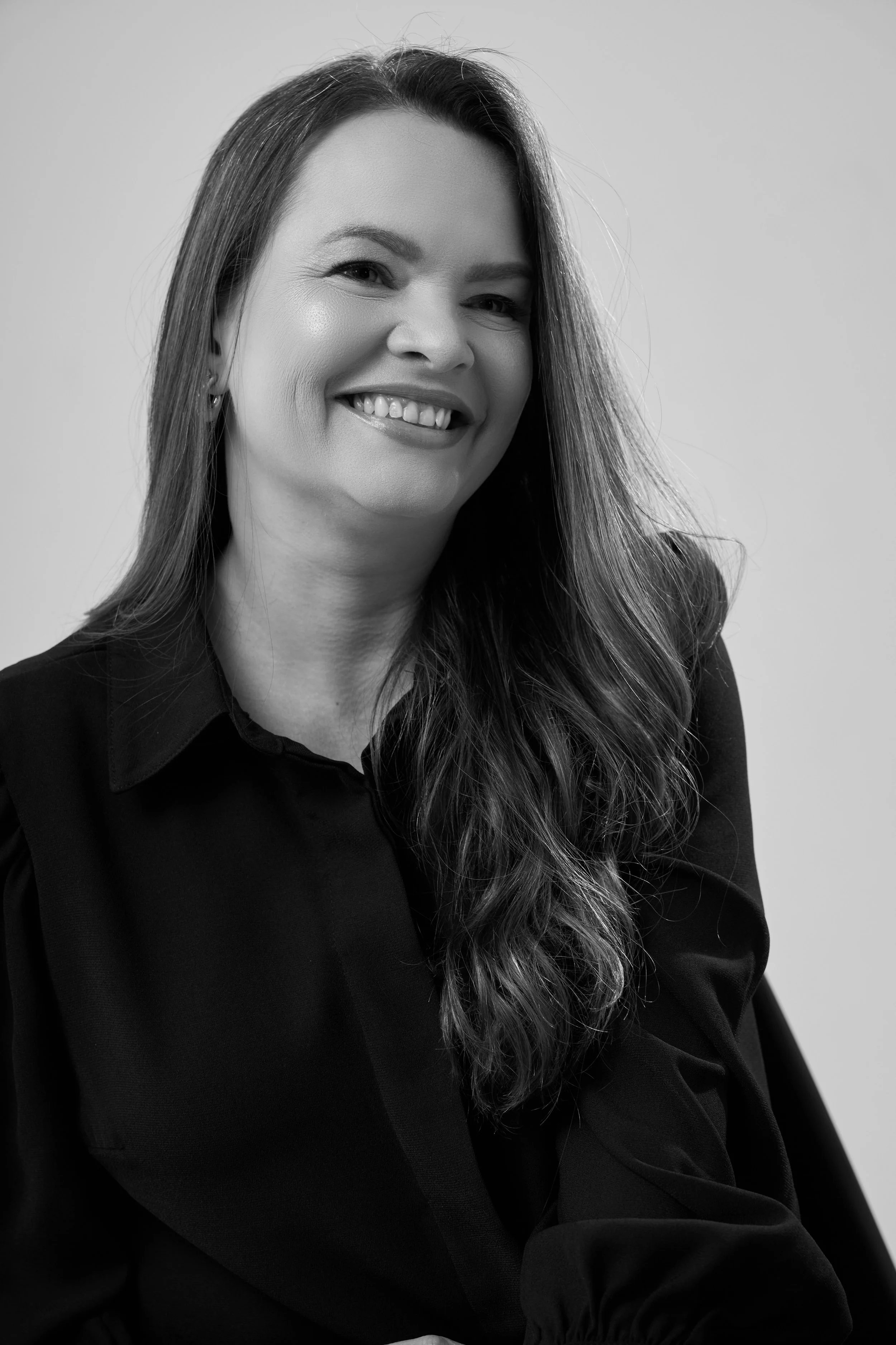 Retrato de uma mulher sorridente com cabelos longos e ondulados, vestindo uma blusa escura, em foto preto e branco.