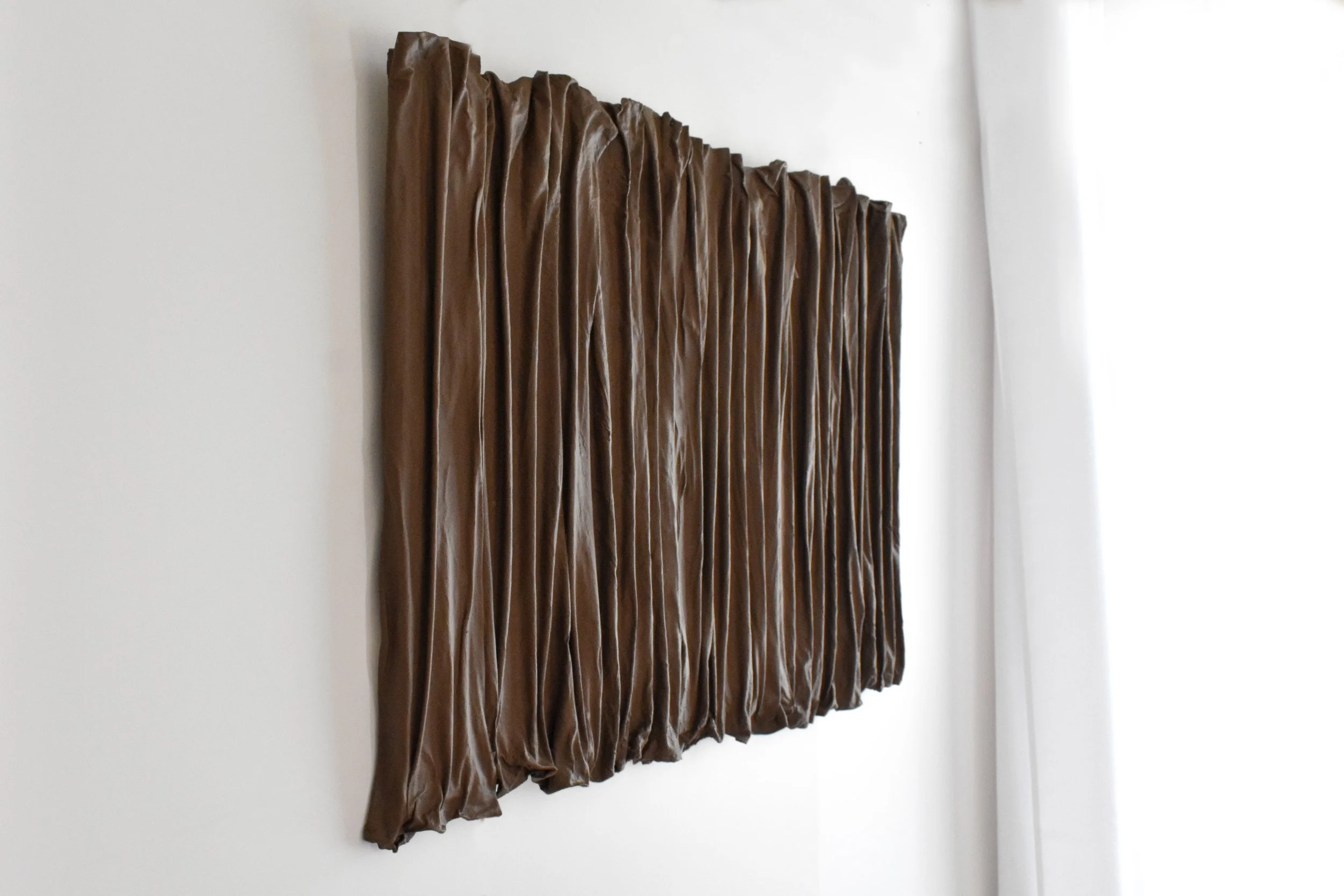 Brown pleated curtain hanging on a white wall beside a white curtain.