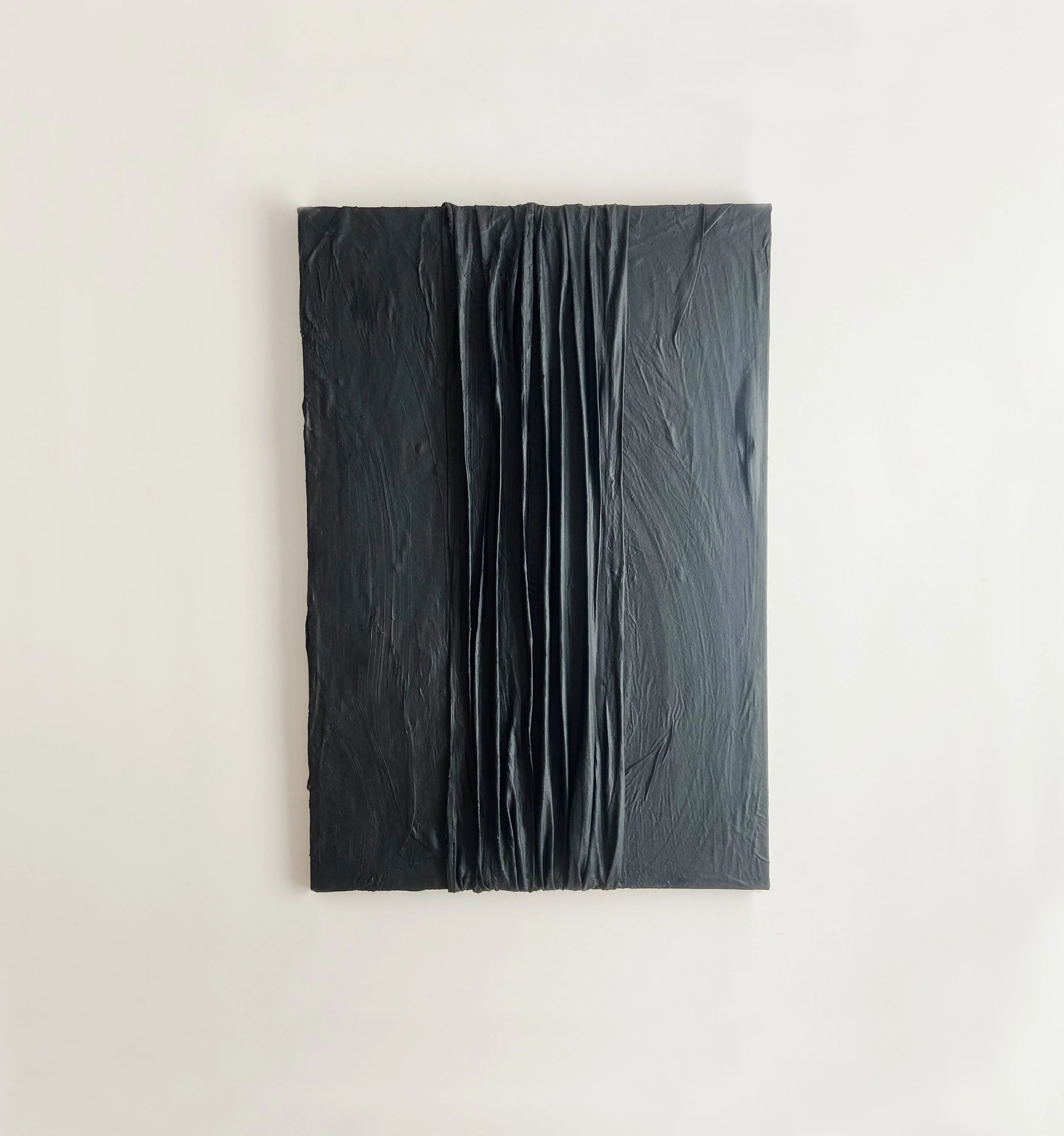 Black textured artwork with vertical draped fabric in the center, mounted on a white wall.