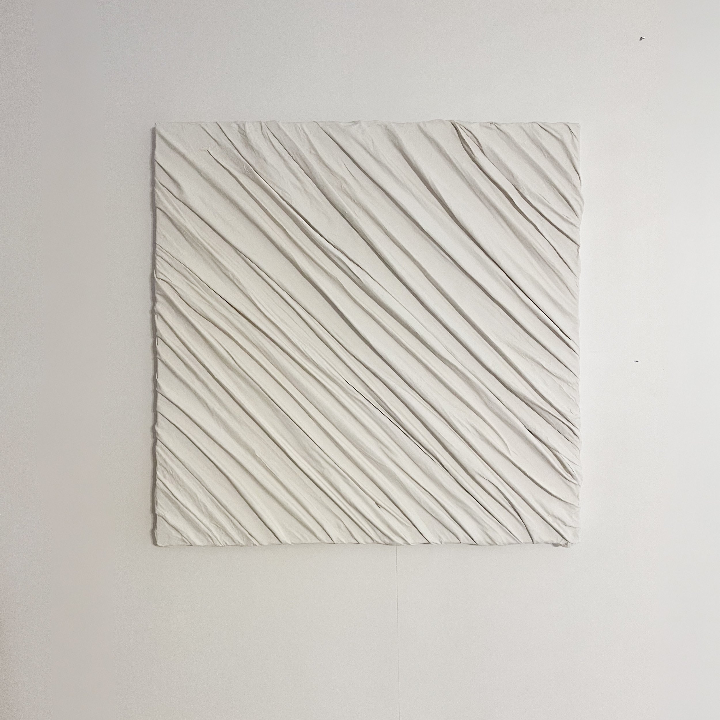 Square white textured wall art with diagonal ridges on a plain white wall.