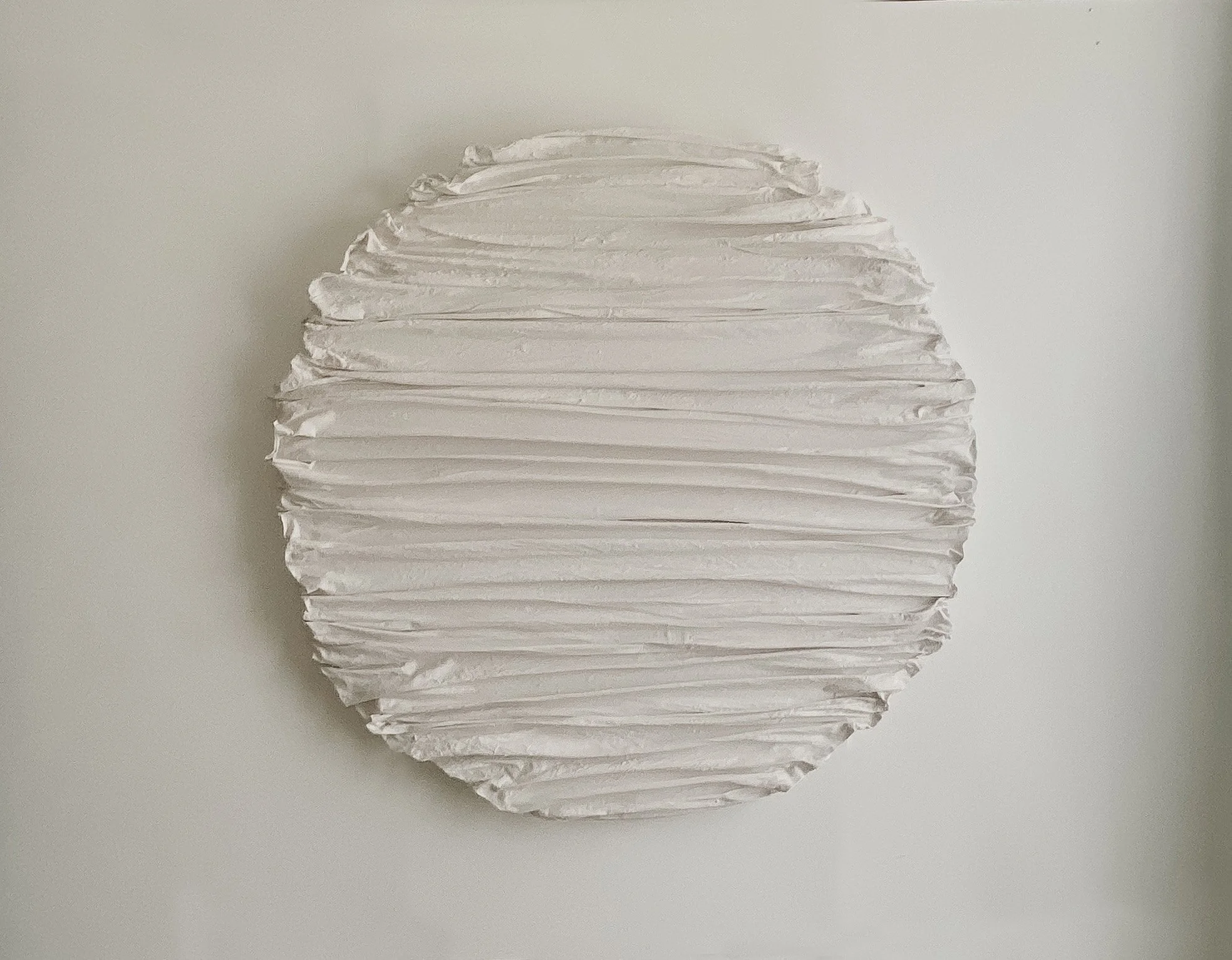 A round, white paper lantern with horizontal ridges, hanging against a plain, light-colored background.