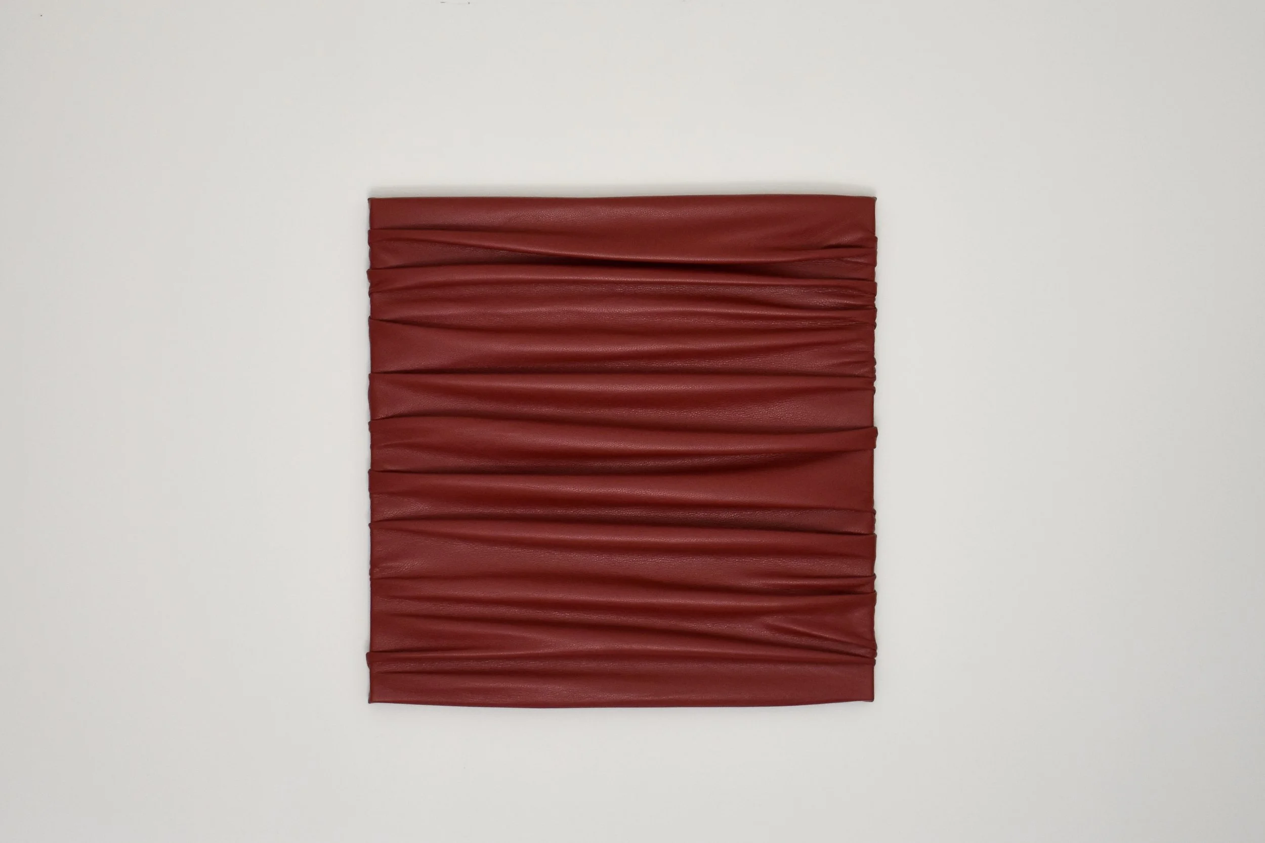 A rectangular piece of red leather with horizontal folds, mounted on a white wall.