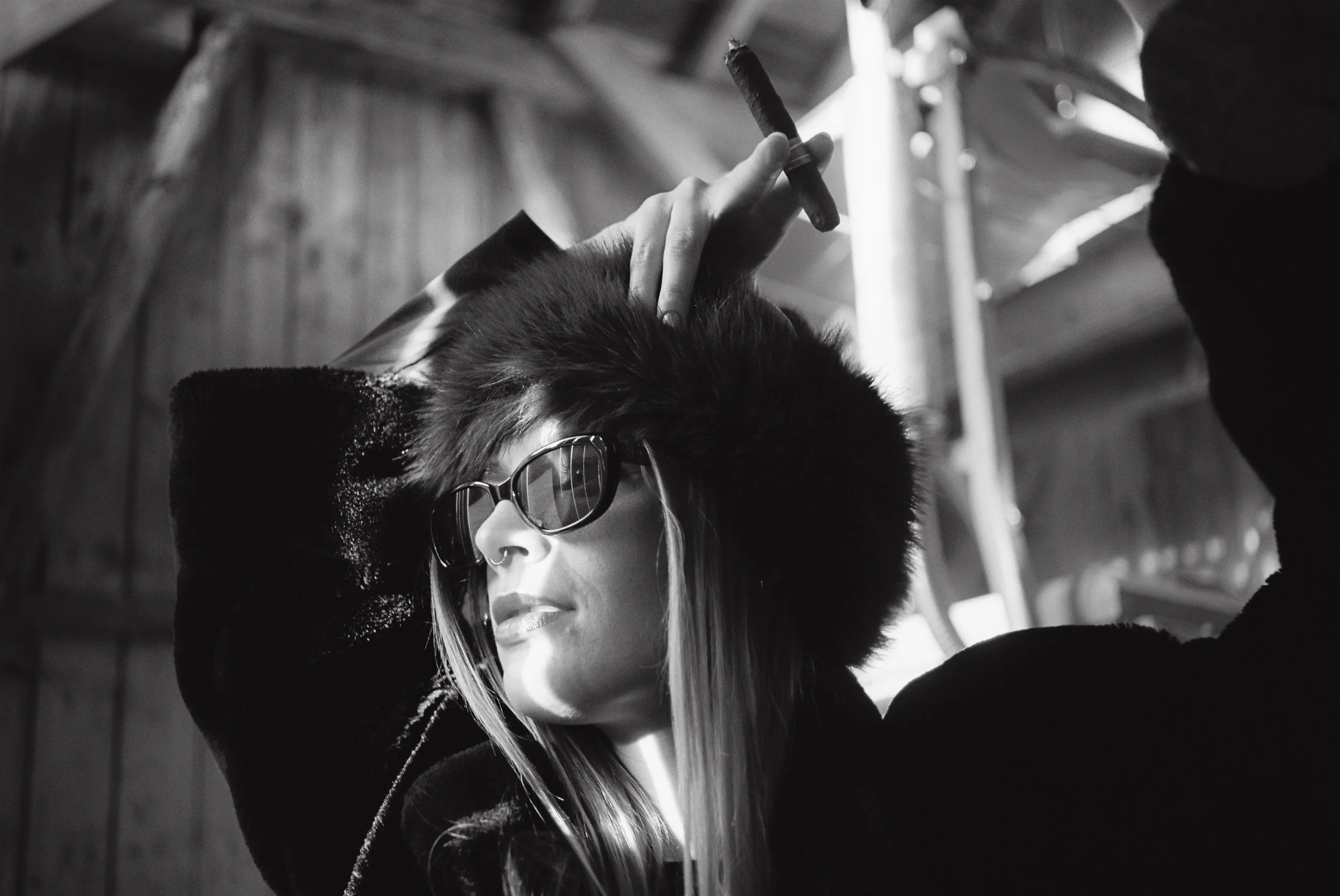 Schwarz-Weiß-Fotografie einer Frau mit dunklen Sonnenbrillen, die einen kleinen Zigarre hält, während sie auf einem Kopf gekippt ist.