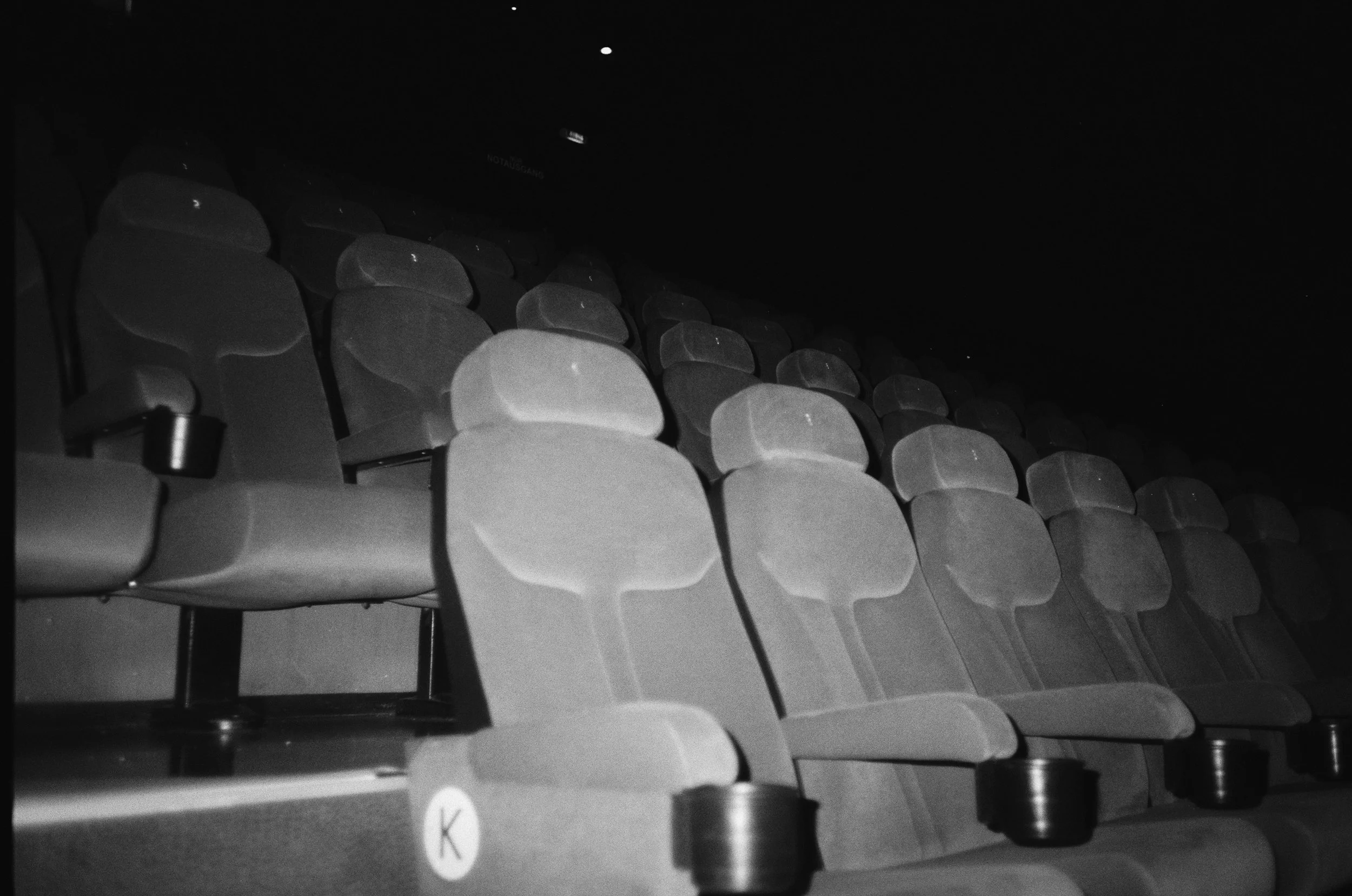 Leere Kinoreihen mit schwarzen Sitzen in einem dunklen Saal.