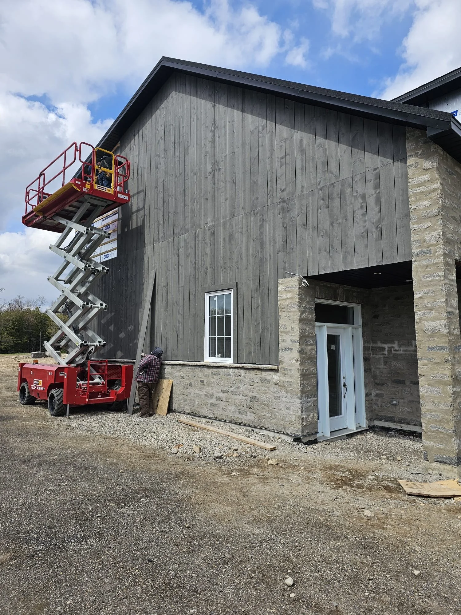 Construction workers installing siding on a building with a scissor lift.