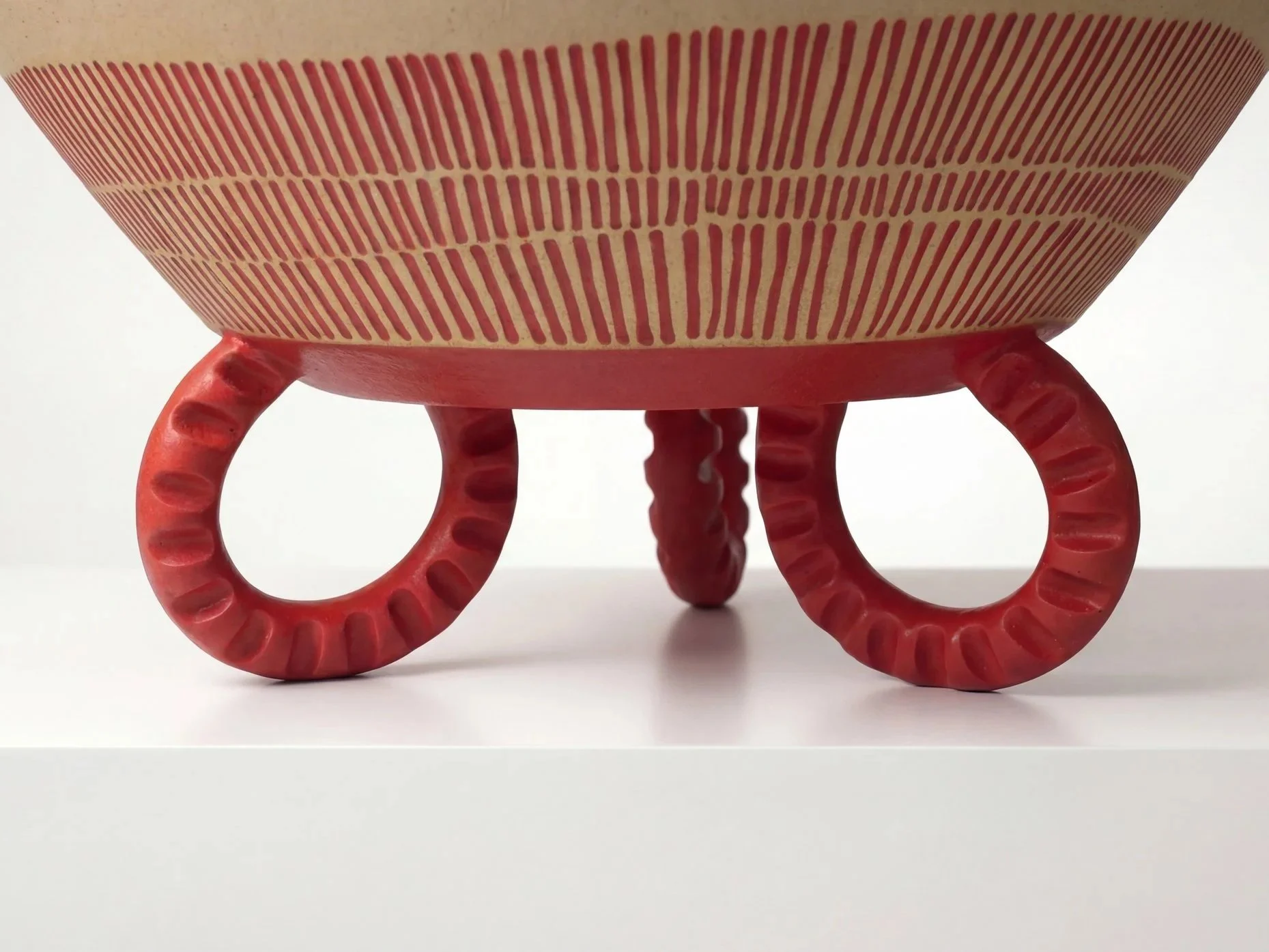 A decorative red and beige striped bowl on three circular legs with textured, spiral-like details.