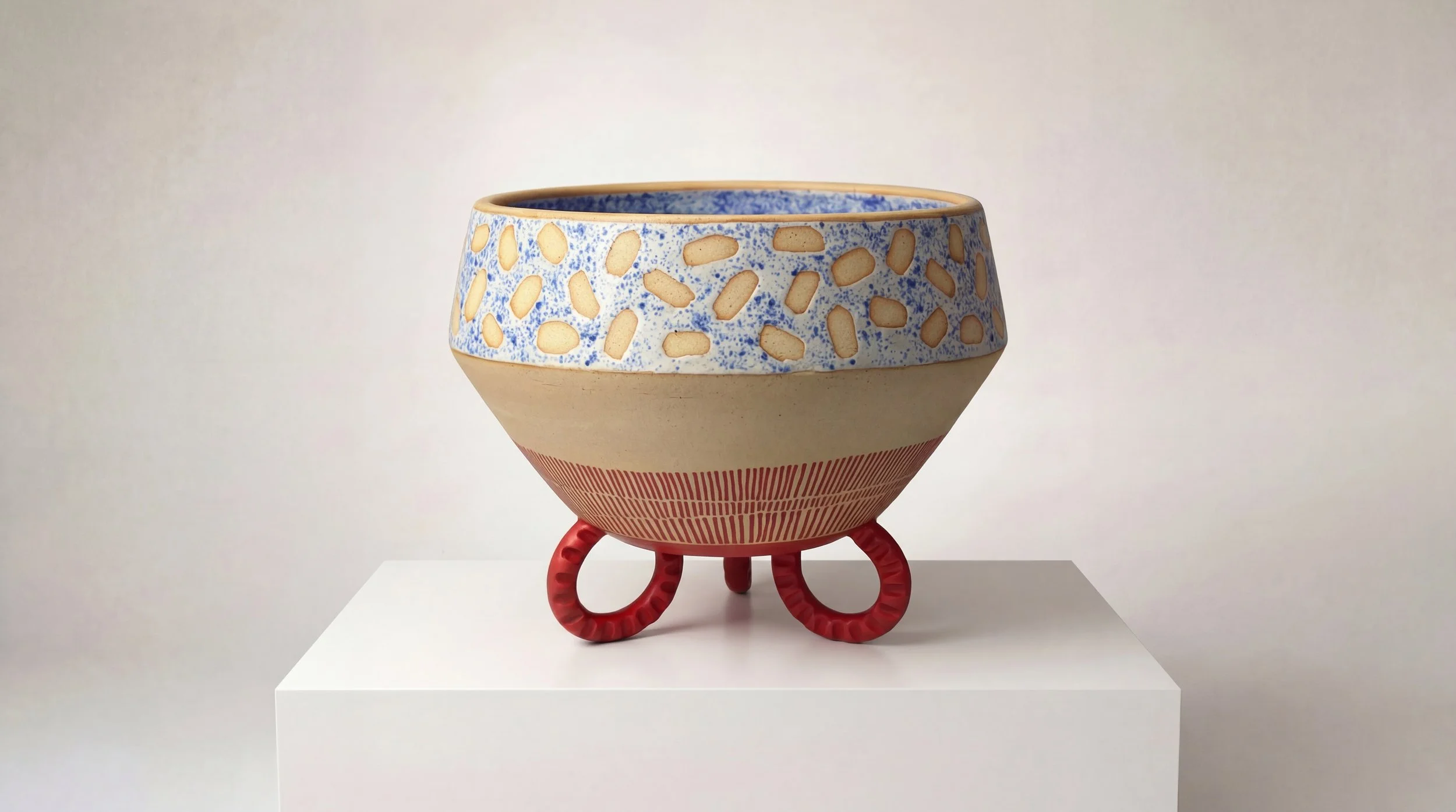 Colorful ceramic bowl on a white pedestal with decorative patterns and red spiral-shaped legs.