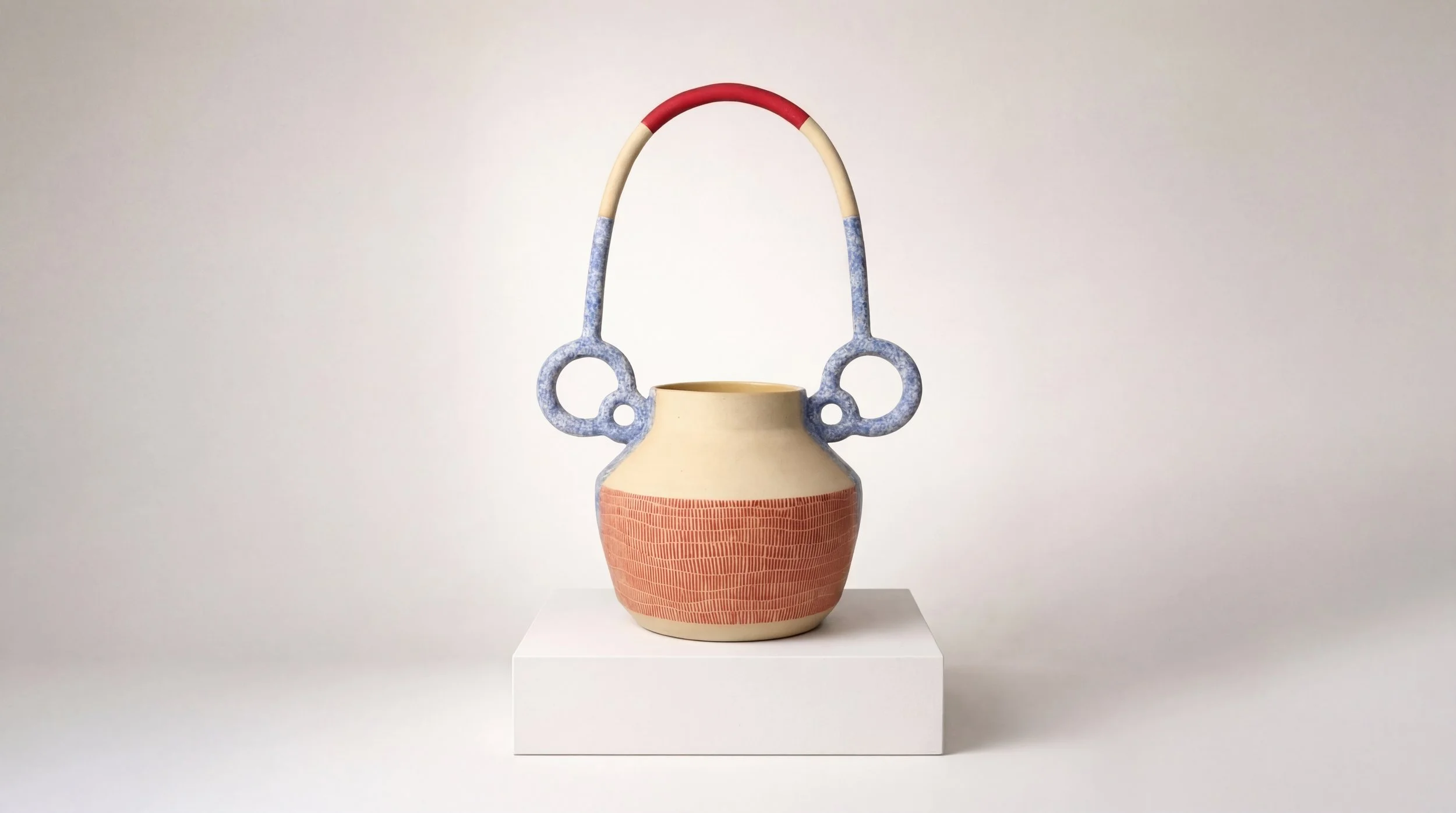 Handmade ceramic vase with a geometric pattern, featuring a wide round base, narrow opening, and a decorative handle with blue, beige, and red accents, placed on a white pedestal against a plain background.
