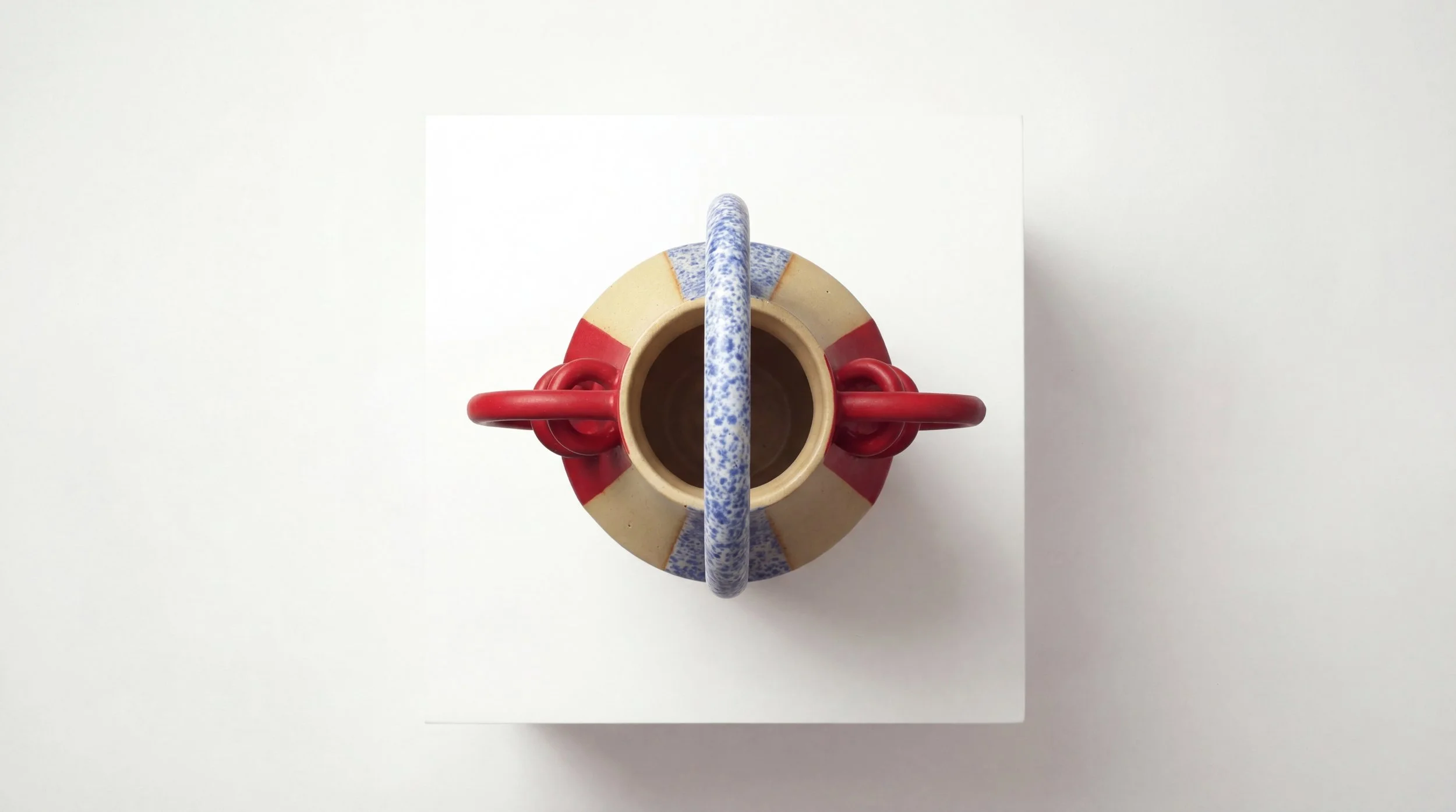 Top-down view of a colorfully decorated ceramic mug with a handle, placed on a white surface.