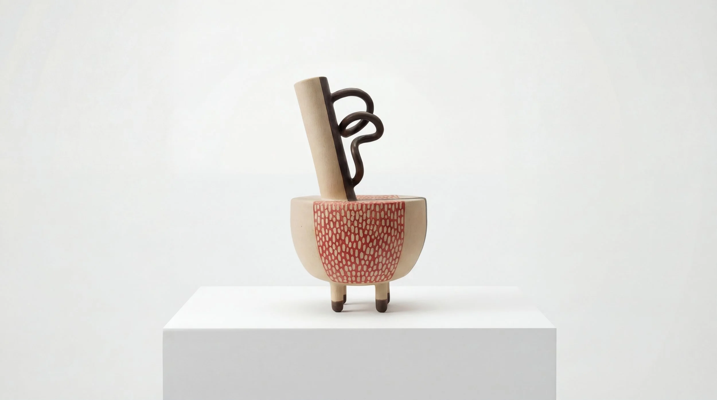 A modern ceramic sculpture with a beige bowl shape, supported by three small legs. The sculpture features a patterned red section and a black abstract vertical element extending outward.