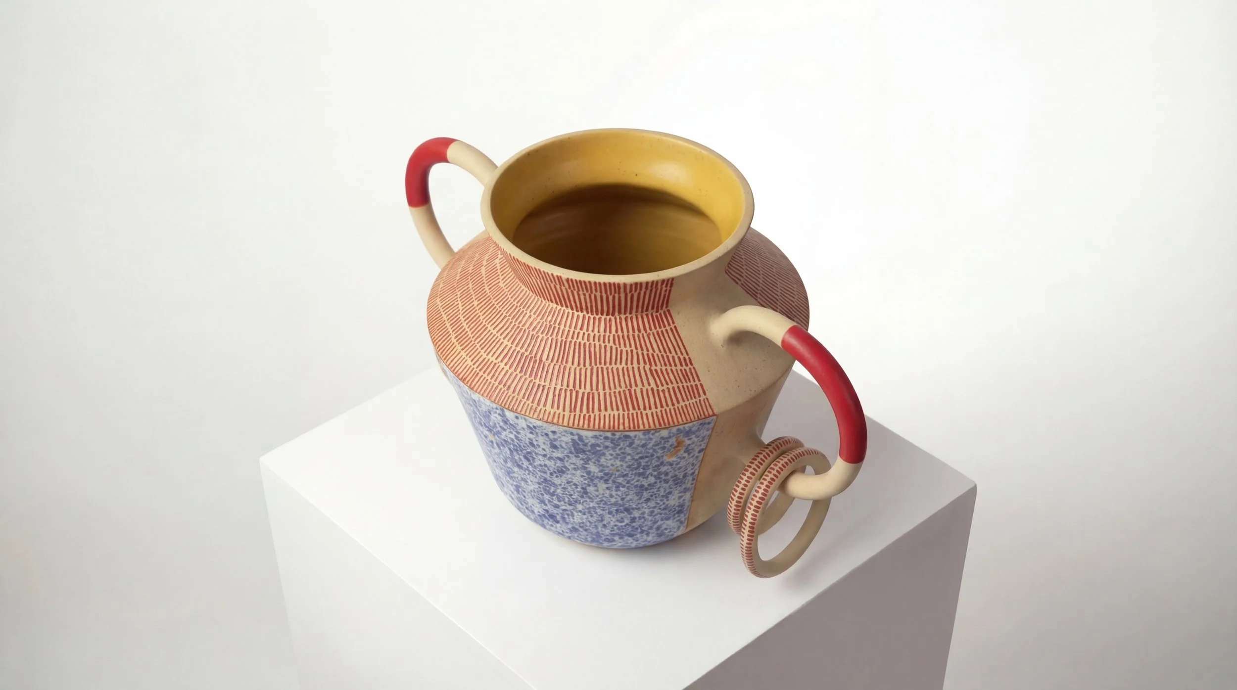 Ceramic teapot with red and white handles, decorated with terracotta and blue patterns, filled with tea, on a white pedestal against a plain white background.