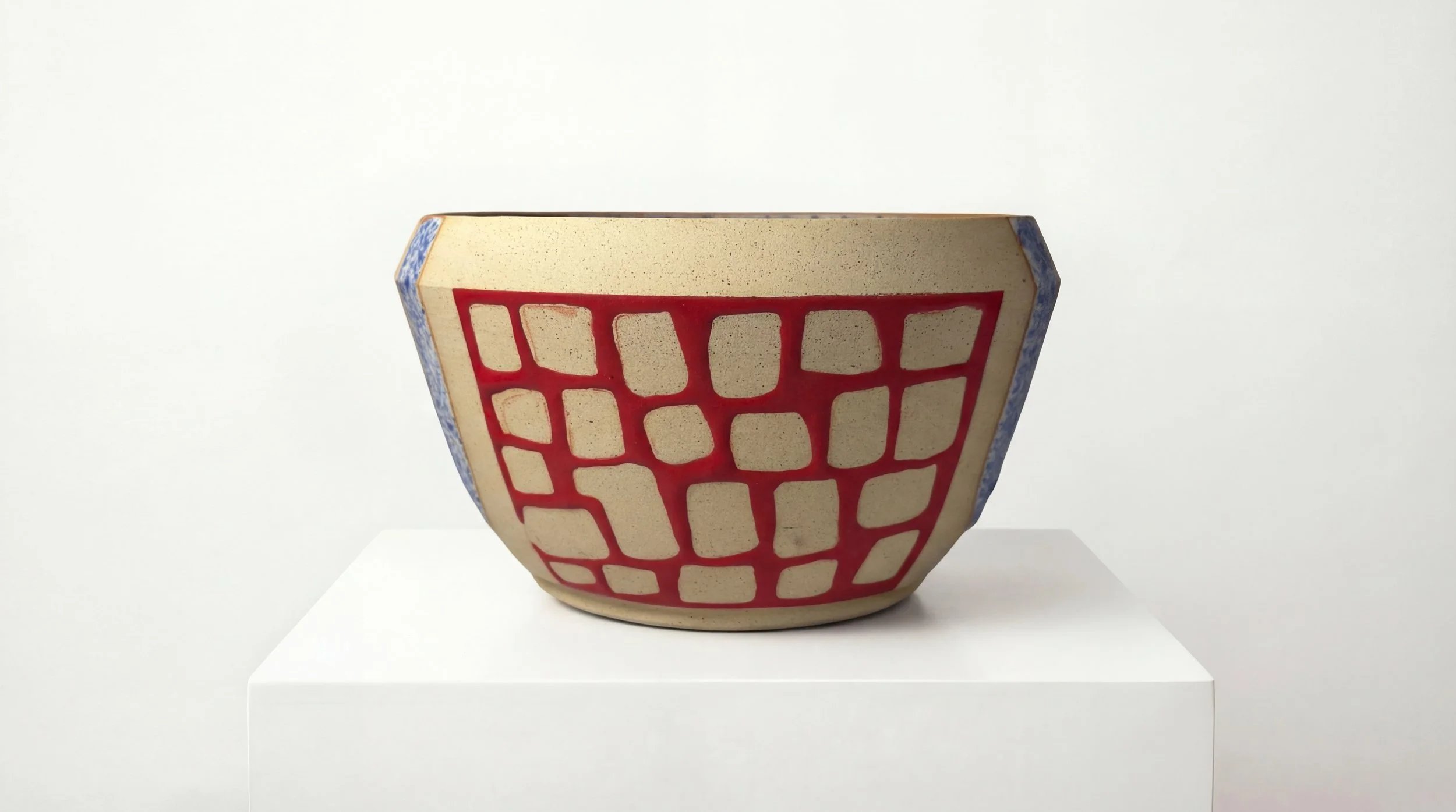Ceramic bowl with red grid pattern and blue accents on a white pedestal against a plain white background.
