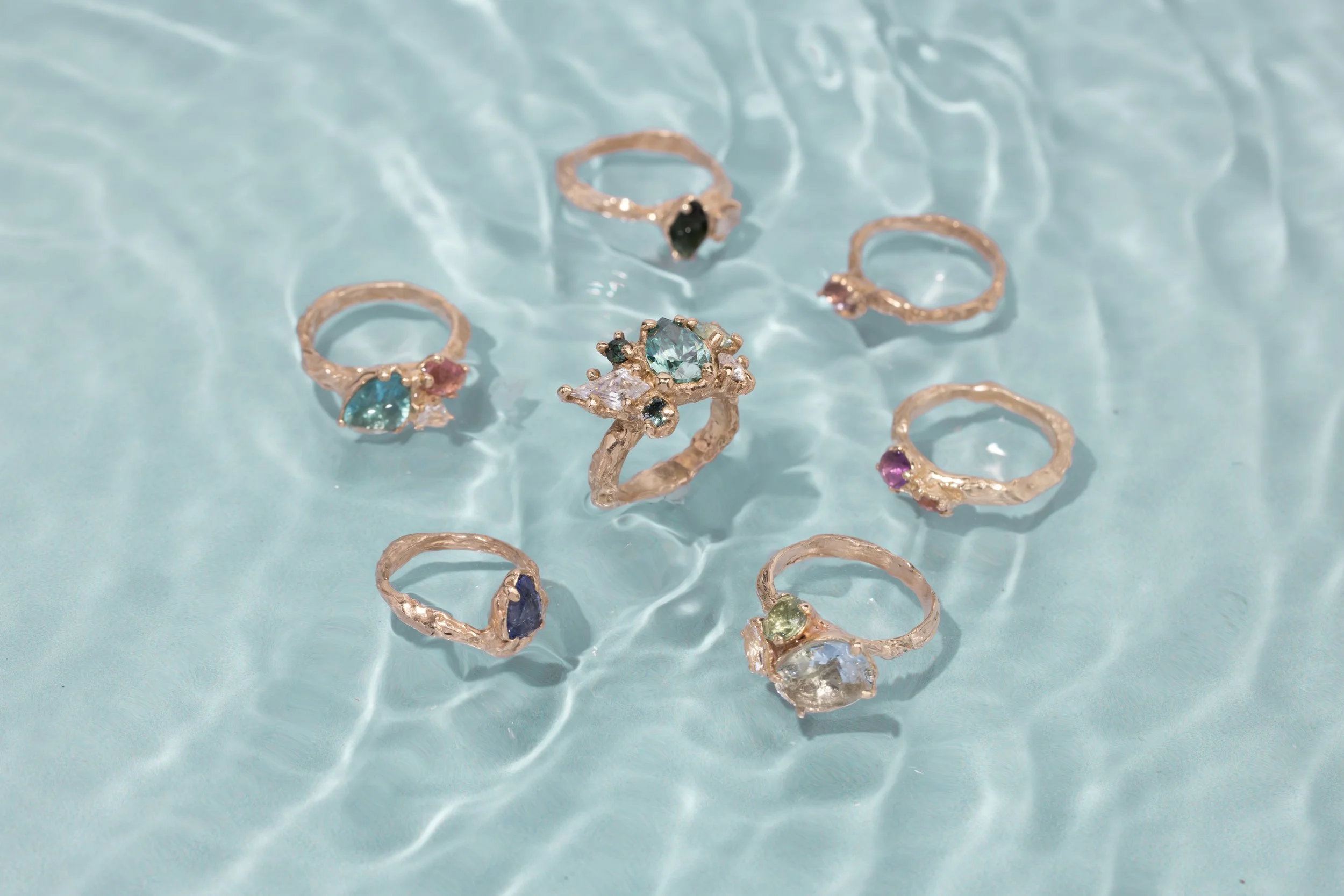 A collection of colorful gemstone rings floating on the surface of water with ripples.