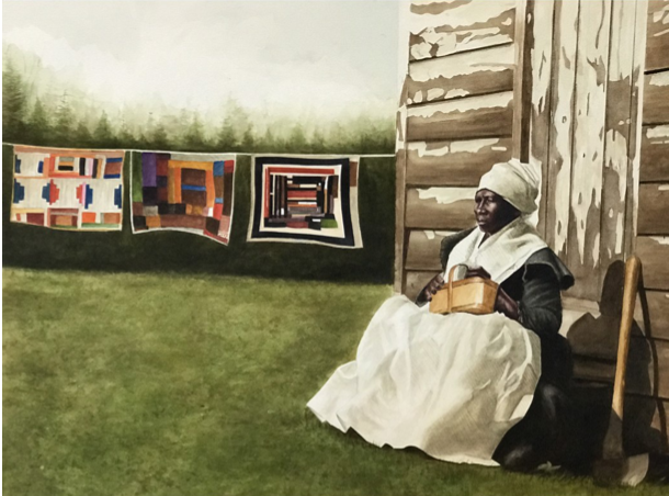 A woman dressed in historical clothing, including a bonnet and white apron, sitting outside against a wooden building next to a chair. Quilts are hanging on a line in the background on a grassy field with trees.