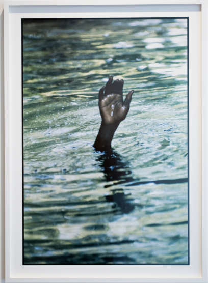 A hand emerging from water, reaching upward, with ripples on the surface.