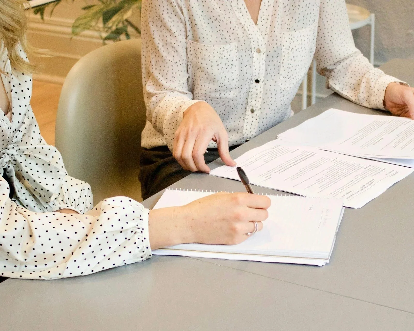 Two people reviewing and signing documents together at a table during a personal organization meeting.
