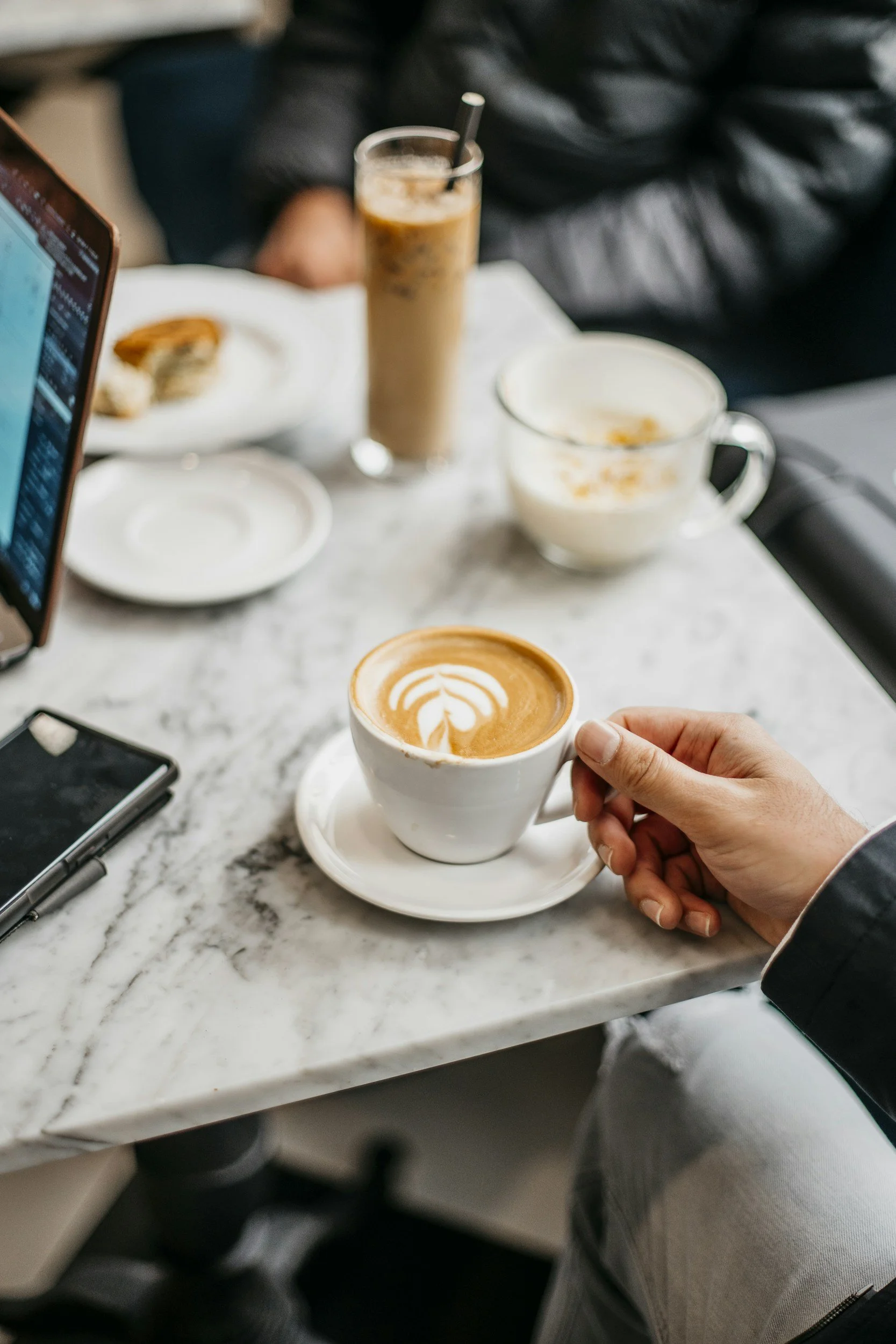 Hand holding a cup of coffee beside a laptop and phone, representing an initial fit call and strategic financial consultation for healthcare founders | Intellichoice Solutions