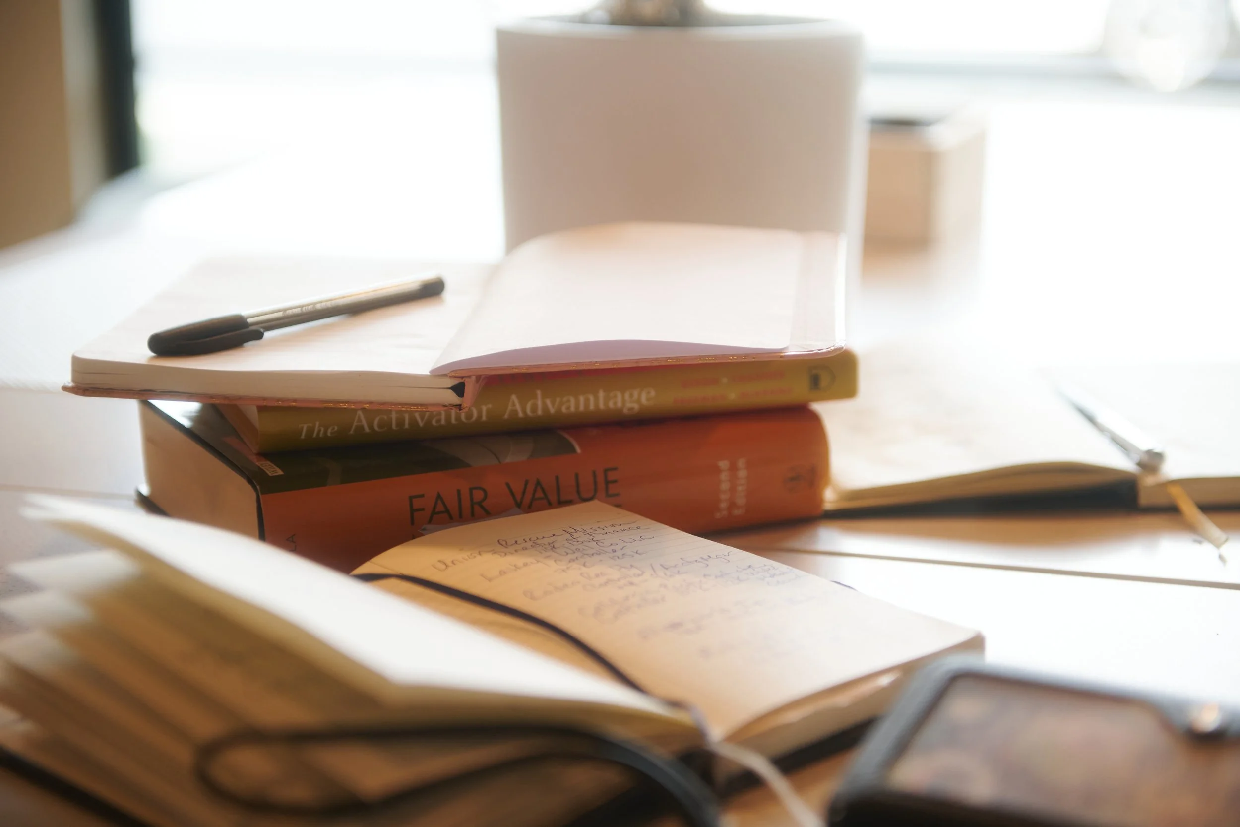 Stacked books and open notebook with handwritten notes representing financial analysis, valuation planning, and strategic clarity for healthcare founders | Intellichoice Solutions