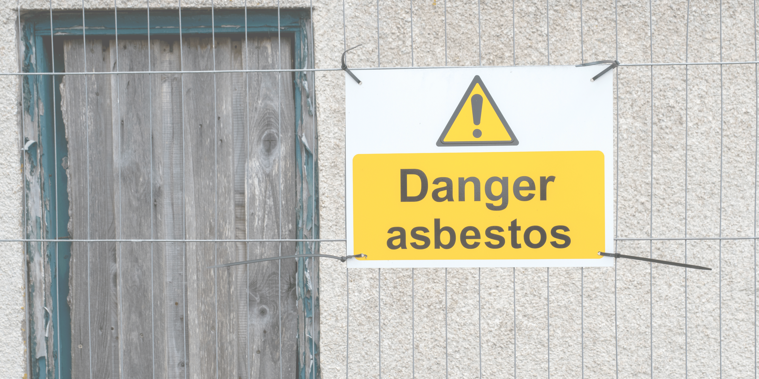 A warning sign on a metal fence reading 'Danger asbestos' in black letters on a yellow background, with a triangle containing an exclamation mark.