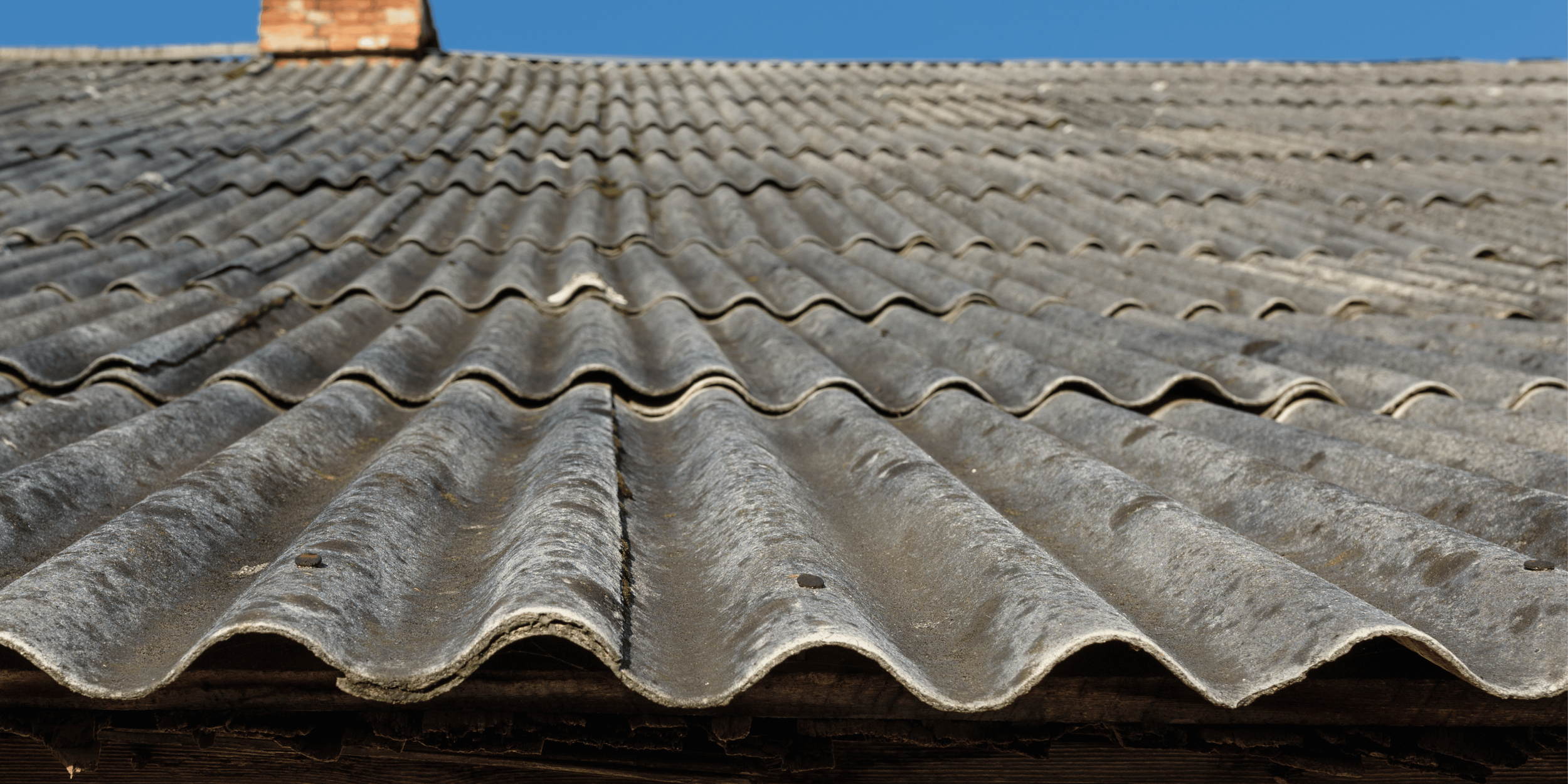Close-up view of aged, weathered gray ceramic roof tiles on a sloped roof with a clear blue sky in the background.