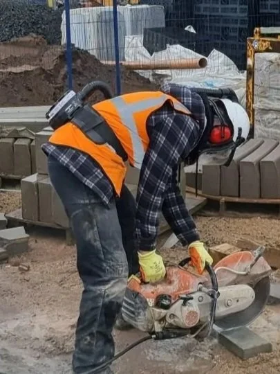 Construction worker in safety gear using a saw on a construction site with brick pavers.