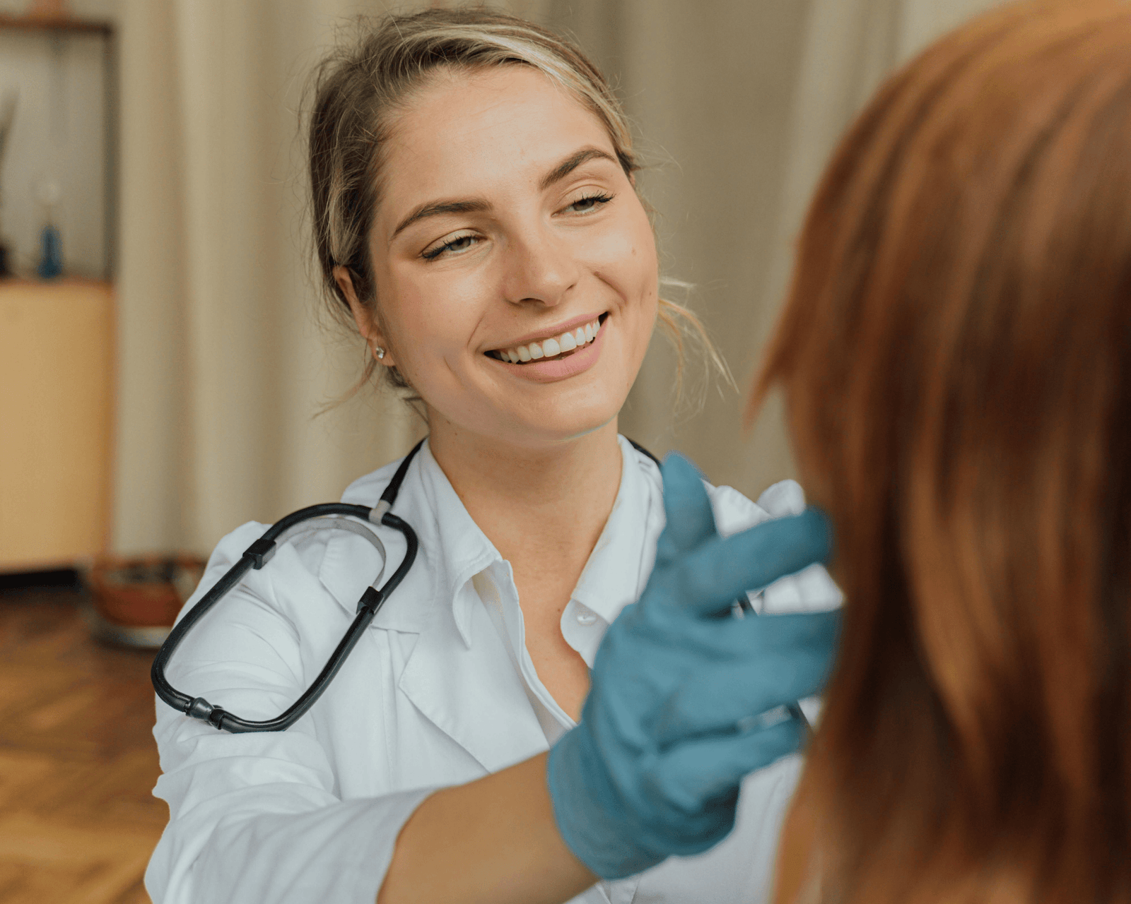 A smiling healthcare professional, wearing a white coat and stethoscope, examining a patient with a friendly demeanor.