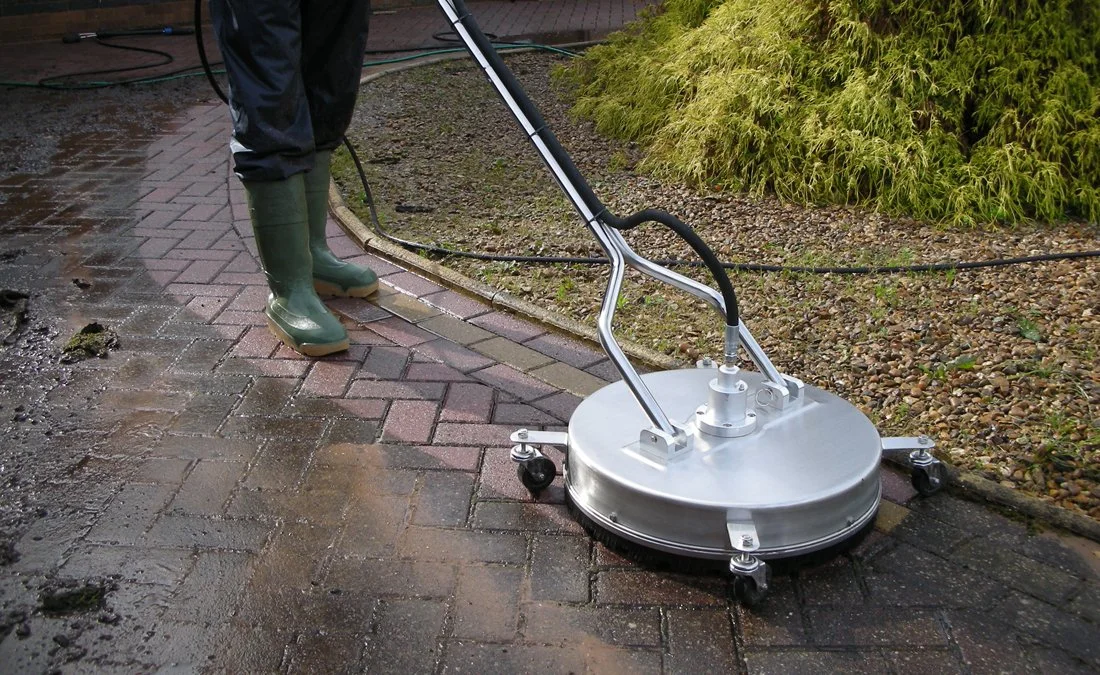 Person using a power washer to clean brick pavement outdoors during rainy weather.