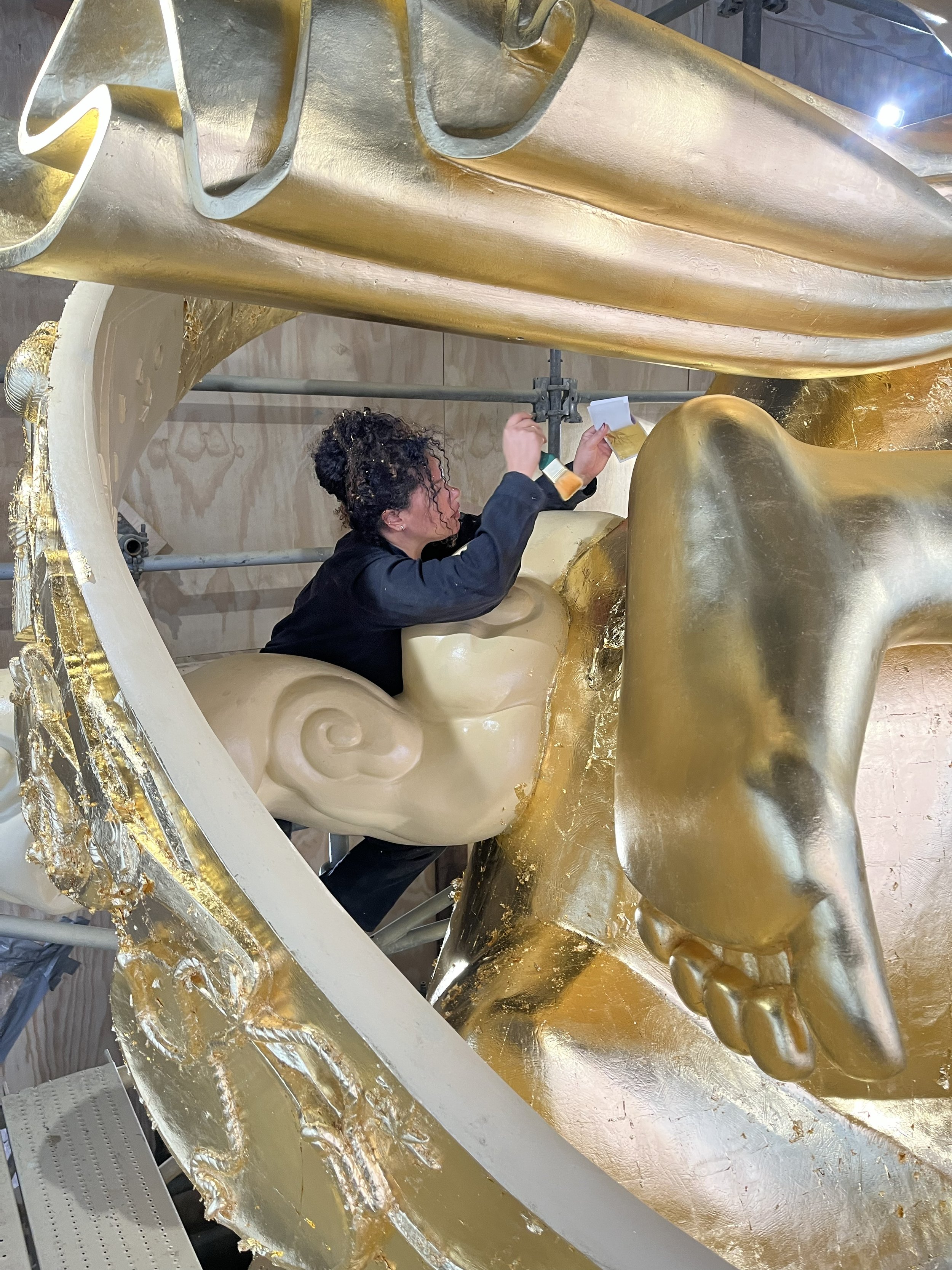 A person working on a large, ornate, golden sculpture with detailed decorative elements.