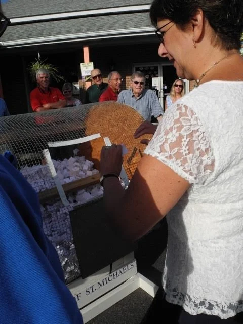 Woman in white lace shirt purchasing baked goods at an outdoor event with a crowd in the background.