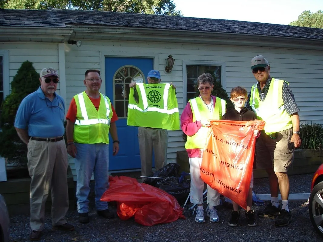 Group of six people standing outside a house, some wearing yellow safety vests, holding a bright orange 