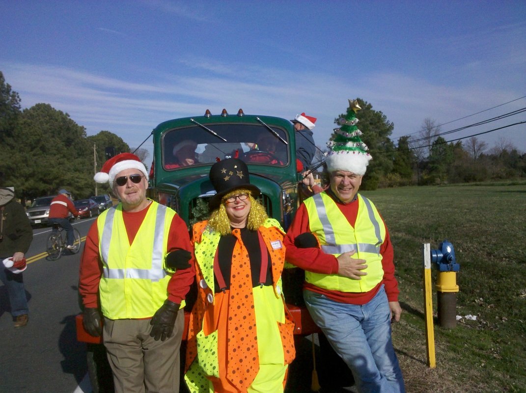 People dressed in festive holiday attire standing in front of a decorated truck, celebrating Christmas outdoors.