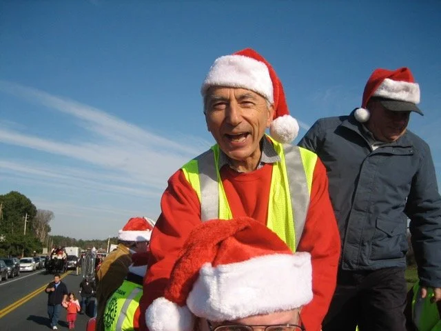 People wearing Santa hats gather outdoors on a sunny day.