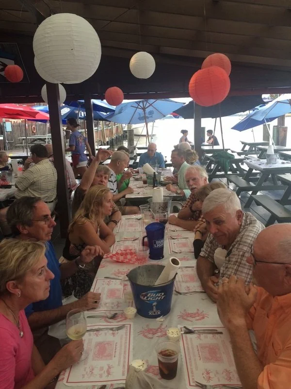 Family and friends gathered at an outdoor restaurant enjoying drinks and conversation, decorated with paper lanterns and umbrellas.